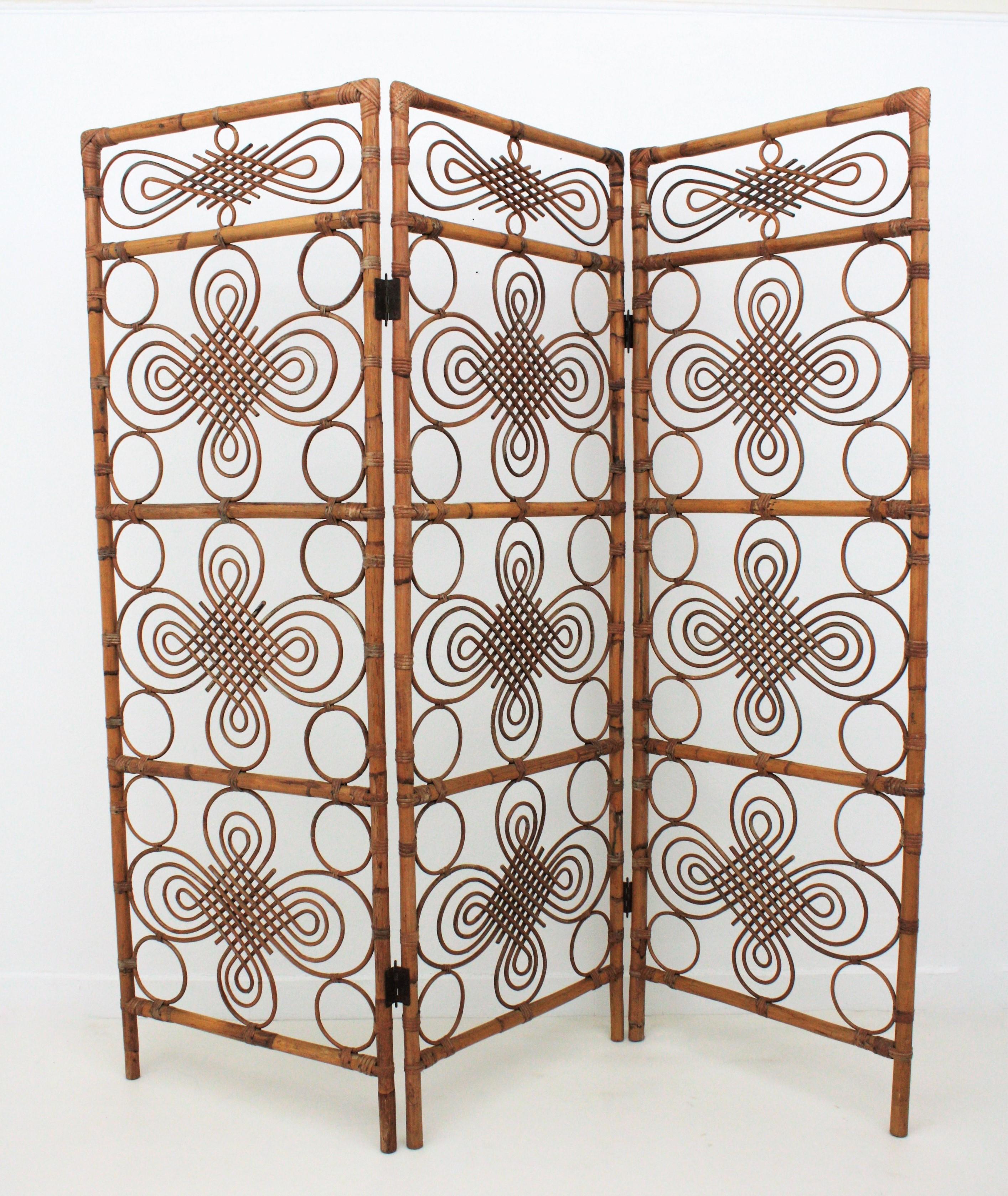Eye-catching handcrafted rattan / wicker and bamboo three-panel folding screen / room divider with filigree decoration. Manufactured in Spain, 1960s.
This rattan folding screen combines Mid-Century Modern and chinoiserie accents.
It can be used as