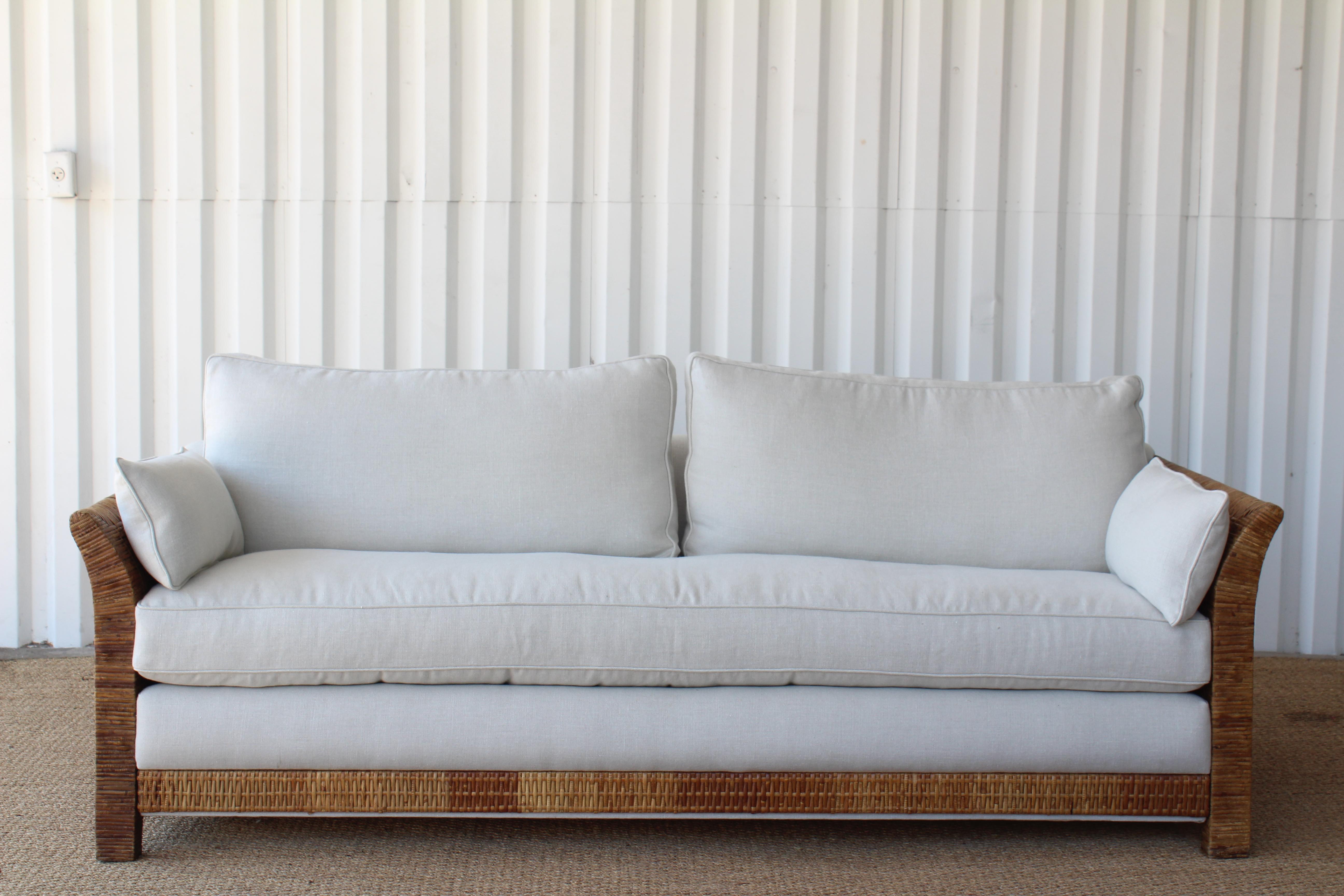 Vintage 1960s rattan framed sofa, newly upholstered in Belgian linen. In good condition with some wear to the rattan frame. Features down-filled pillows.