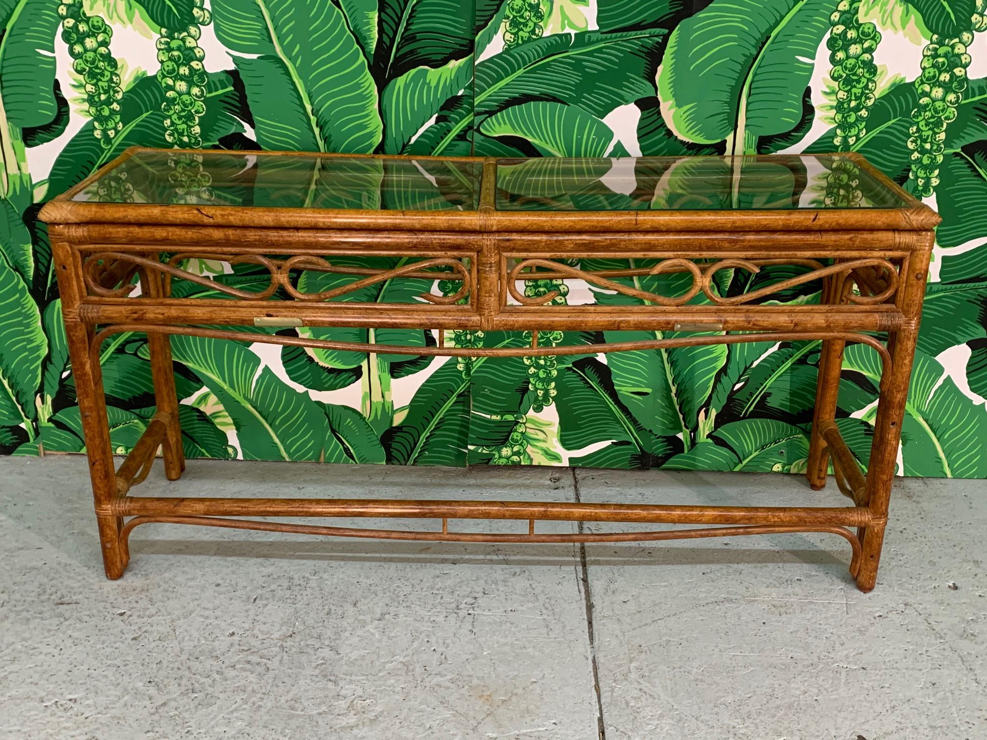 Rattan console table features brass detailing and glass top. Perfect touch of tropical decor to any room. Good condition with minor imperfections consistent with age.