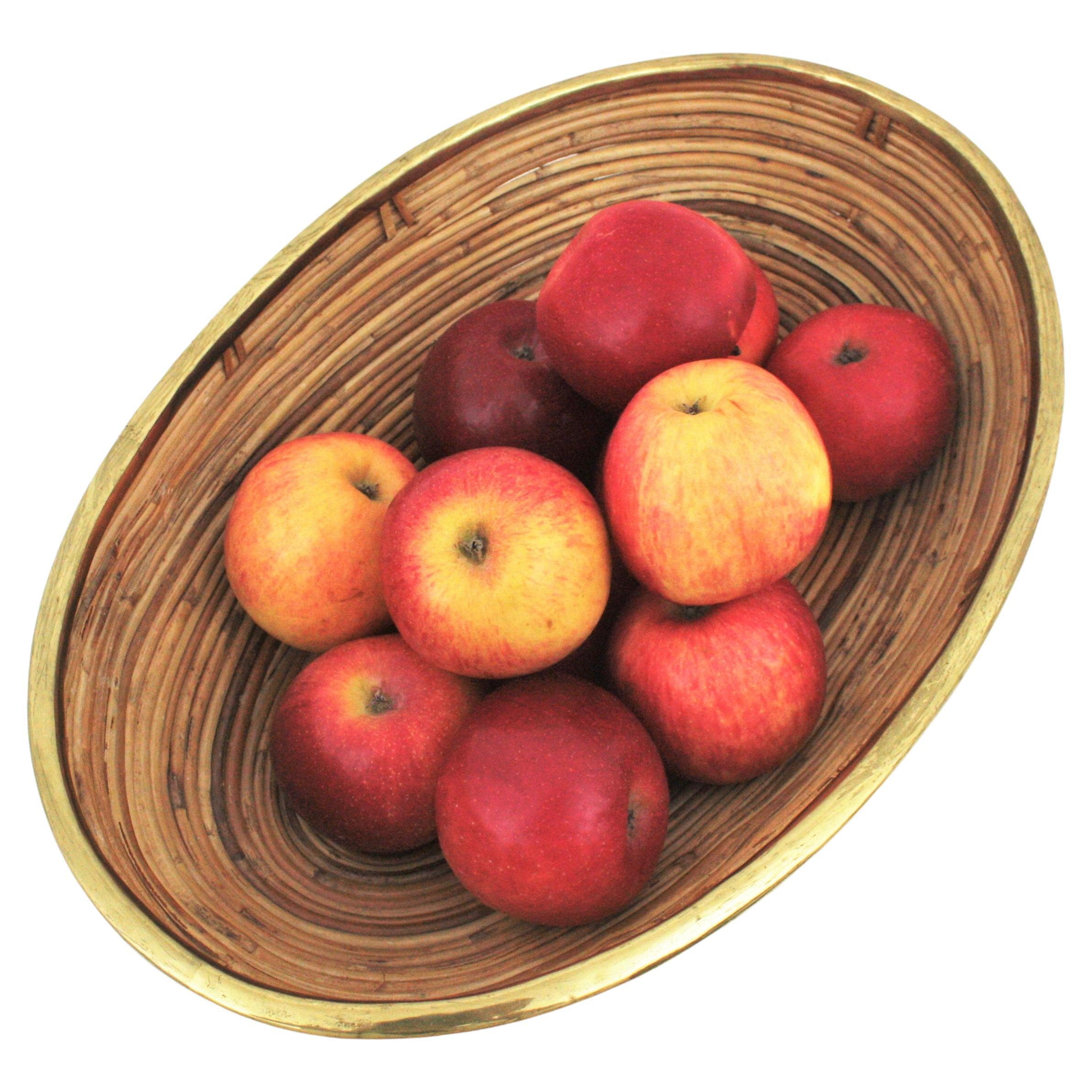 Mid-Century Modern brass and bamboo / rattan large oval bowl, centerpiece or basket.
It has a brass trim covering the top.
Handcrafted in Italy, 1970s. 
Use it as fruit bowl or centerpiece to add a stylish Midcentury accent in a kitchen. Perfect to