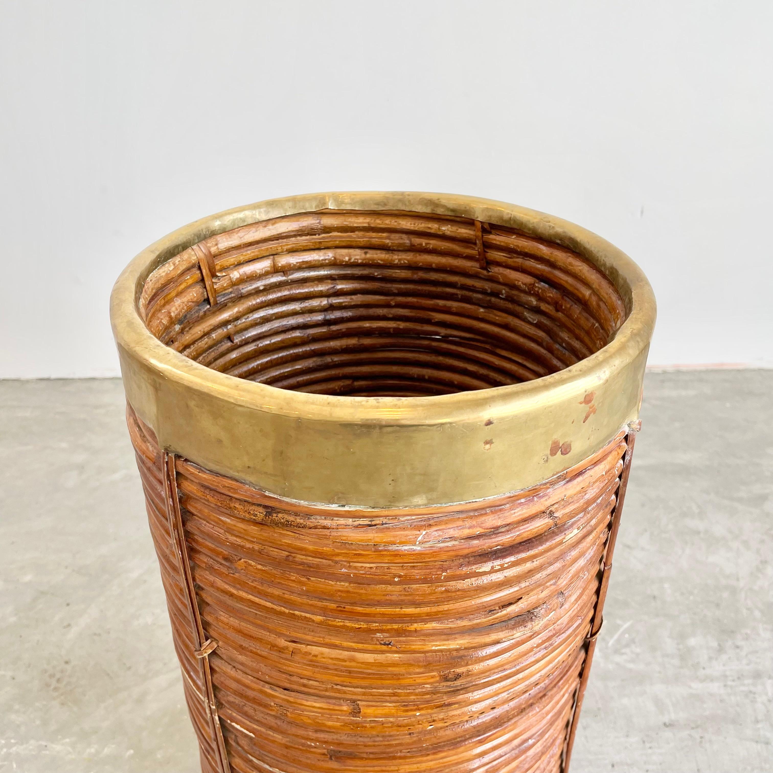 Gorgeous rattan and brass umbrella holder in the style of Gabriella Crespi. Rattan pieces are wrapped tightly in a circle with a thick brass lip around the top. Rattan is woven together with wicker ties as well as glued together. Great sculptural