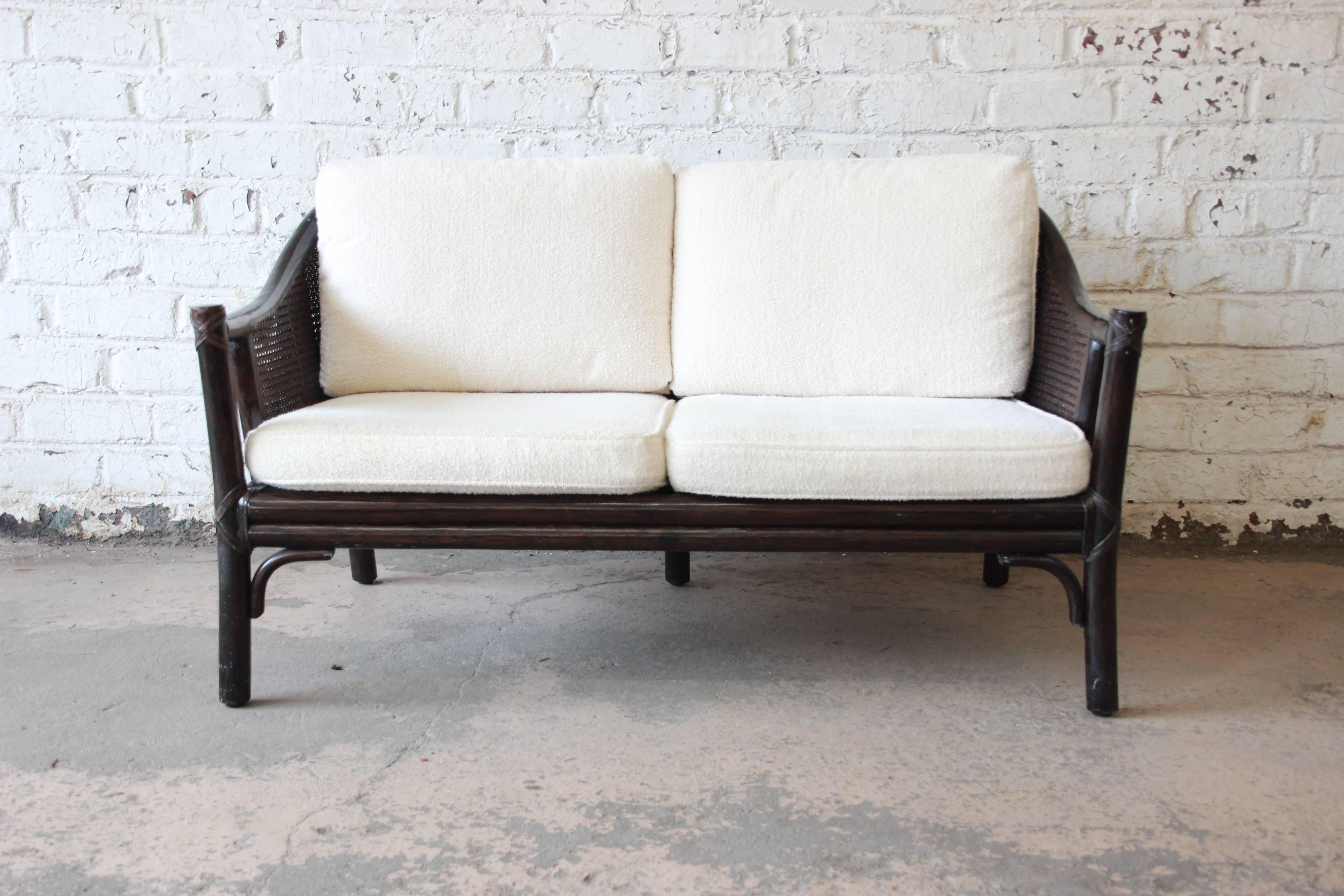 A gorgeous vintage rattan and cane settee or love seat by McGuire. It features expertly crafted hardwood and rattan construction, with a nice patina from age. Caning is all intact, and the ivory upholstery is clean and ready for use. Retains the