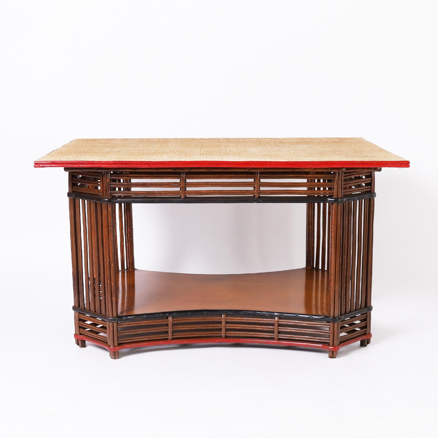 Impressive 1930s art deco table having a grasscloth top over a rattan or stick wicker base highlighted in red and black with a mahogany lower tier.