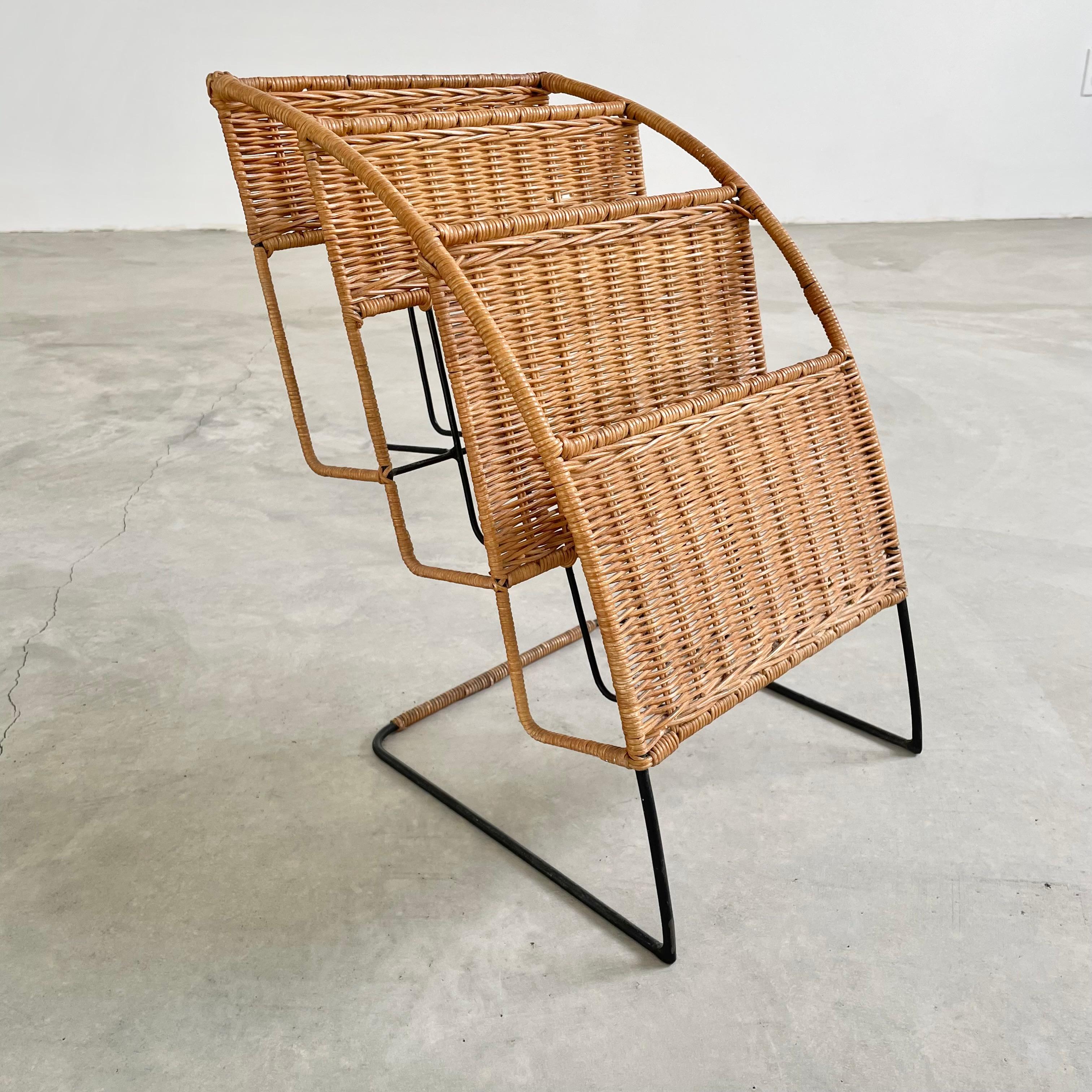 Rattan, wicker and iron magazine rack attributed to Jacques Adnet. Iron frame wrapped with wicker accents and trays. Three angled metal trays to hold magazines or books. Great sculptural piece. Good vintage condition.