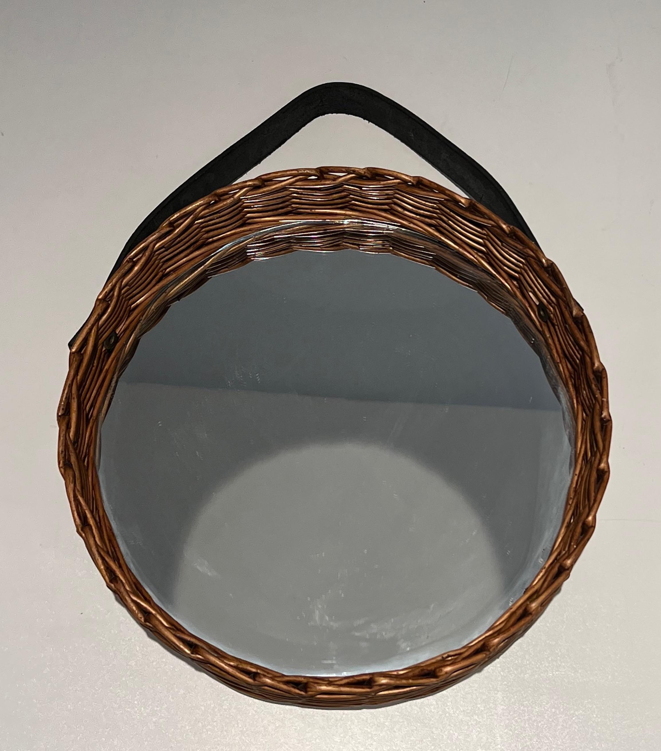 This unusual round mirror is made of a rattan piece surrounded the round mirror with a leather band on top. This is a French work, circa 1950.