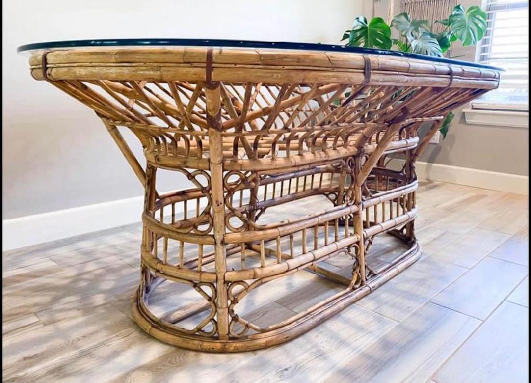 Wonderful oval racetrack shaped rattan dining table. The exposed joints are reinforced with leather rawhide strapping. This table is vintage and a wonderful example of the late mid-century modern Hollywood regency styles. The table sits 6-8 as a
