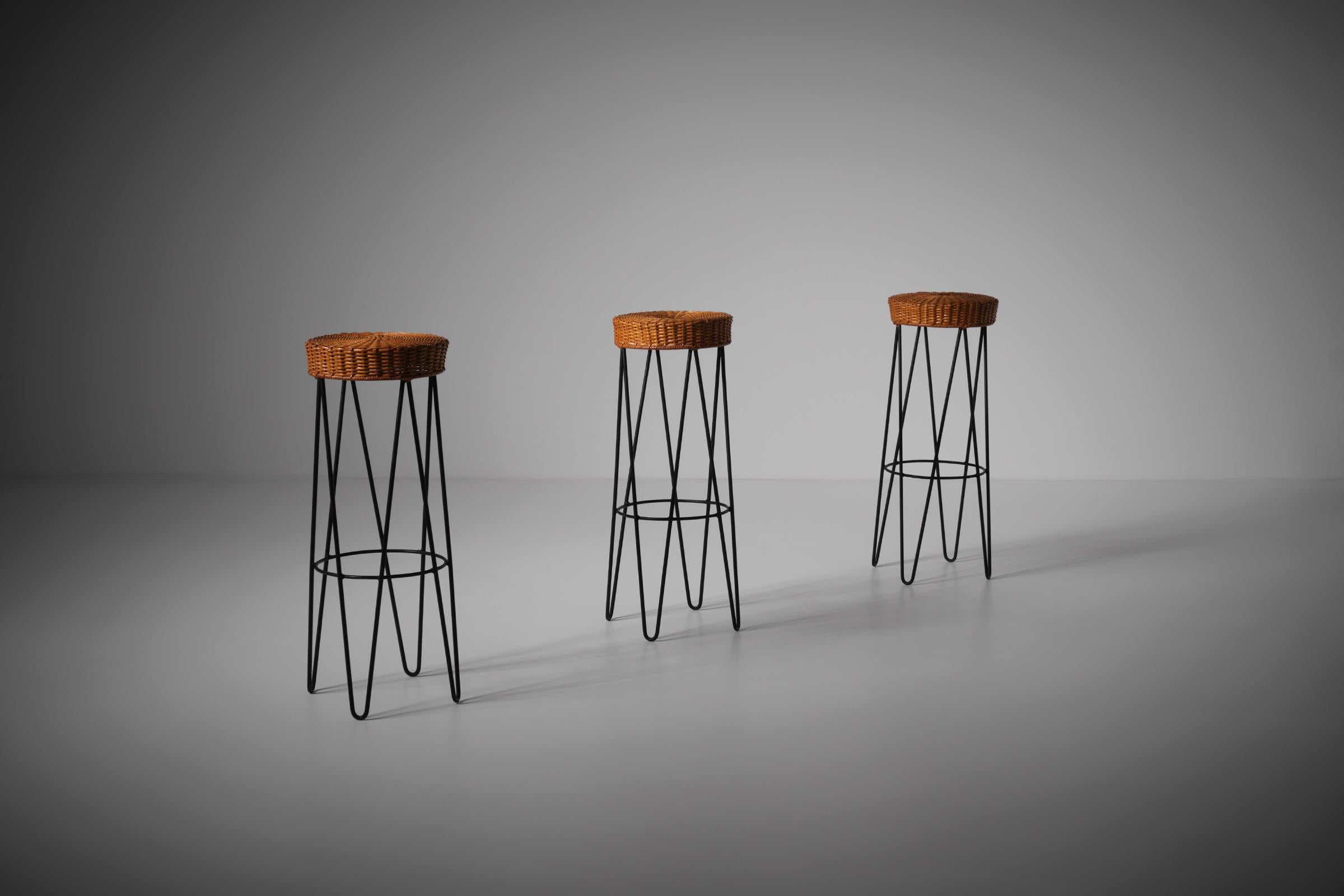 Set of three bar stools, France 1950s. The stools have a nicely woven rattan seat and elegant black metal hairpin frames. The stools are solid and strong and offer a good comfort due to the round circle to rest your feet. In very good original