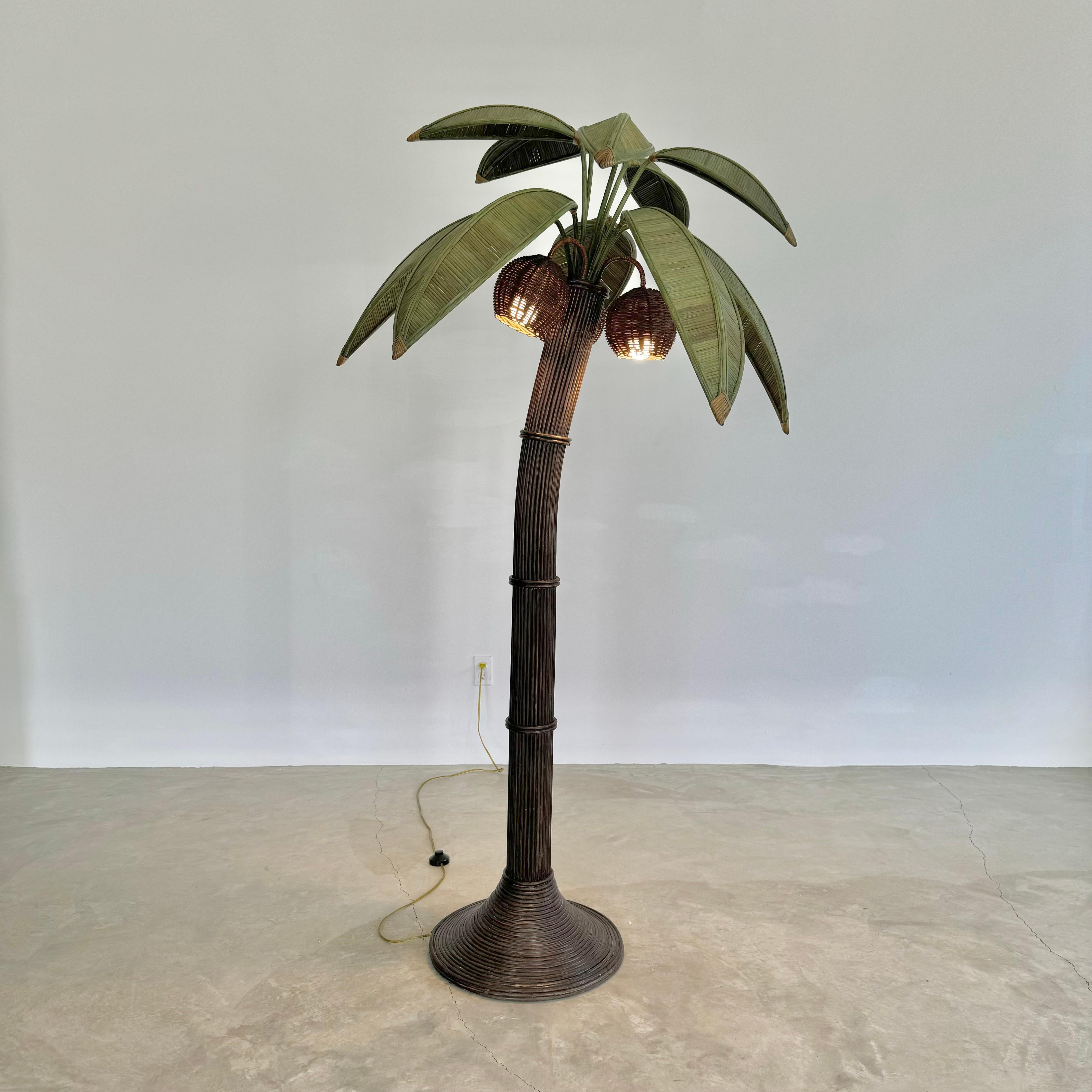 Beachy floor lamp of a palm tree. Original lamp made in the 1970s. Just under 7 feet tall. Made of rattan and wicker and darkened bamboo. Curved trunk resembles a leaning palm tree. Three wicker coconuts each contain a socket/light inside. Coconuts