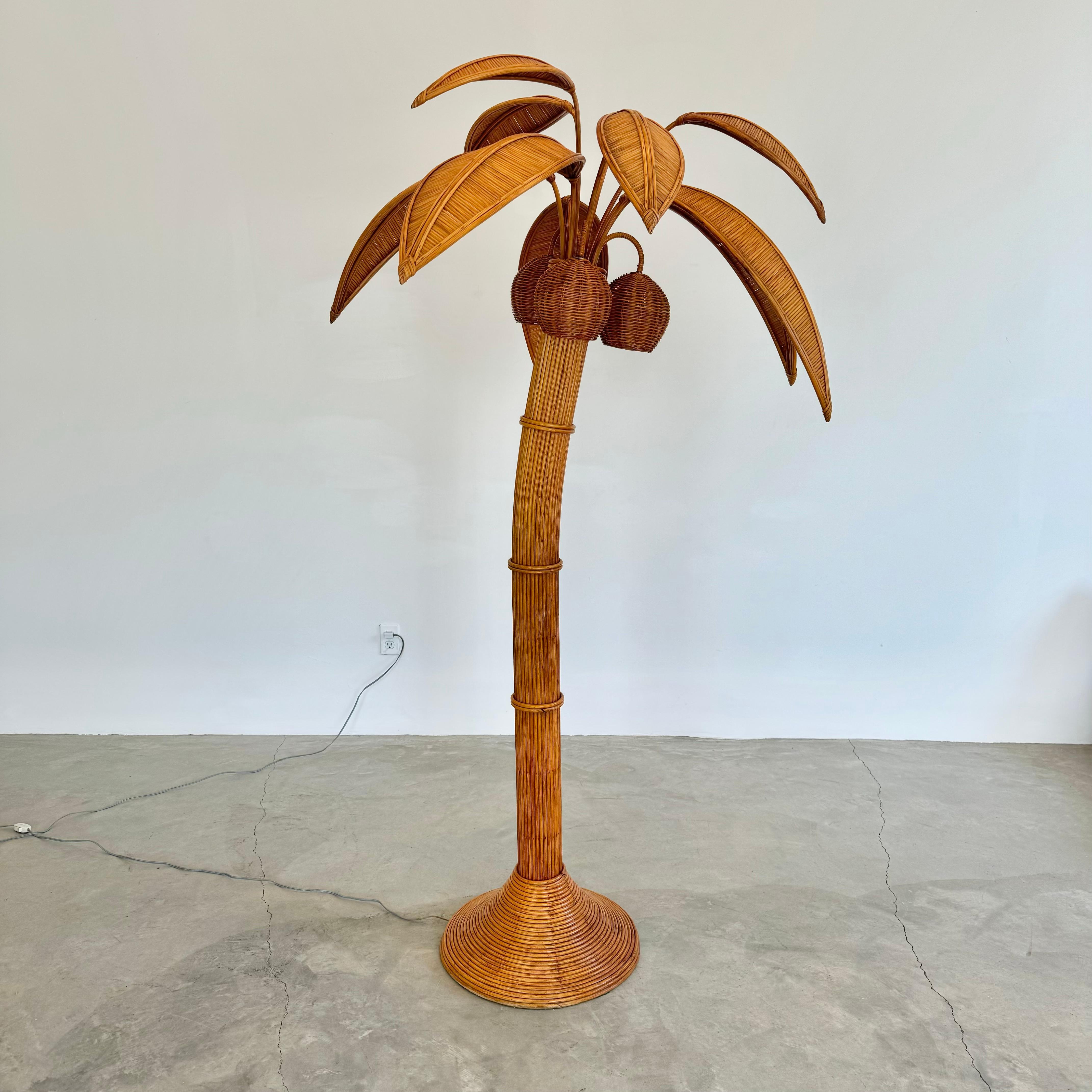 Beachy floor lamp of a Palm tree. Just under 7 feet tall. Made of rattan and wicker. Three wicker coconuts each contain a socket/light inside. Coconuts swivel. Natural color palm leaves made of wicker and rattan sprout out from the top. 5 large