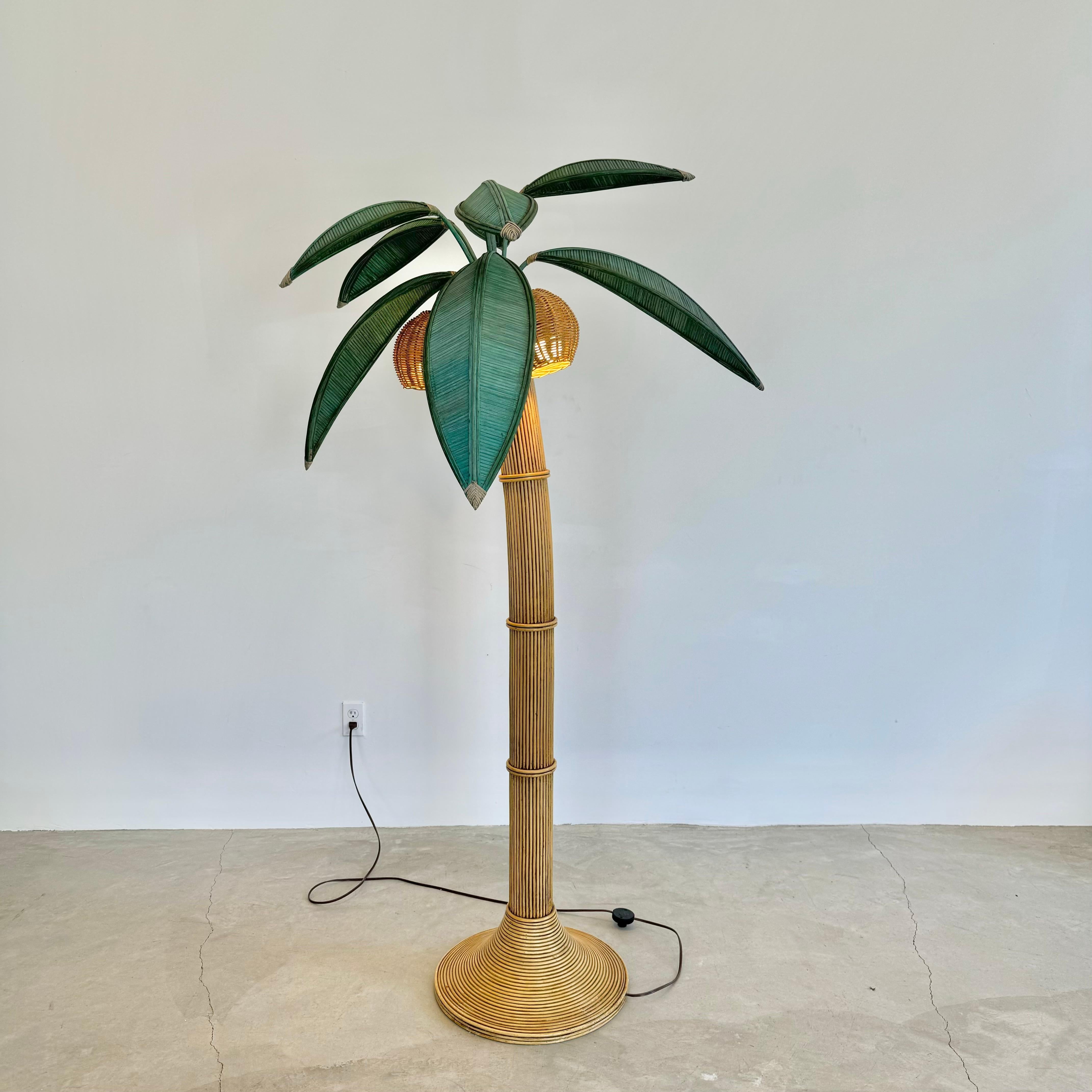 Lampada da terra da spiaggia raffigurante una palma. Lampada originale realizzata negli anni '70. Alto poco meno di 2 metri. Realizzato in rattan, vimini e bambù. Il tronco curvo ricorda una palma inclinata. Tre noci di cocco in vimini contengono