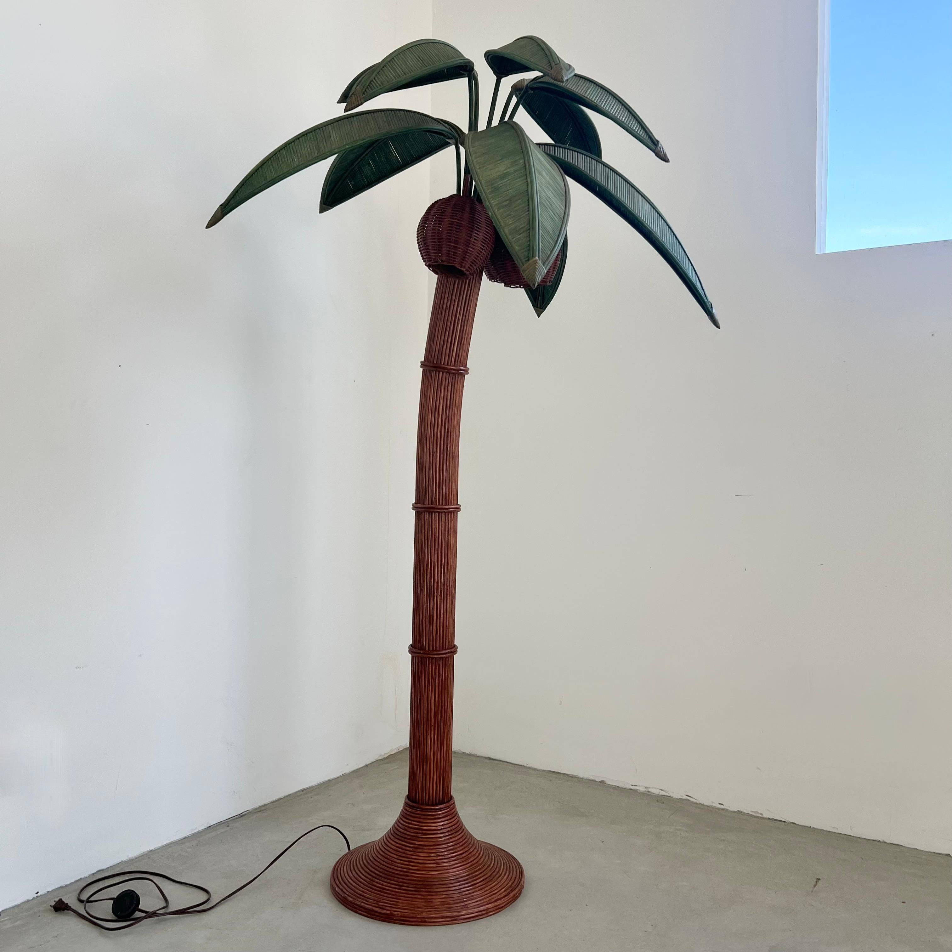 Beachy floor lamp of a palm tree. Original lamp made in the 1970s. Just under 7 feet tall. Made of rattan and wicker and bamboo. Curved trunk resembles a leaning palm tree. Three wicker coconuts each contain a socket/light inside. Coconuts swivel.