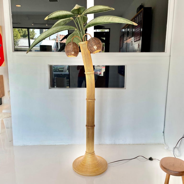 Beachy floor lamp of a Palm tree. Just under 7 feet tall. Made of rattan and wicker. Three wicker coconuts each contain a socket/light inside. Coconuts swivel. Palm leaves made of wicker and rattan sprout out for the top. They rotate 180 degrees as