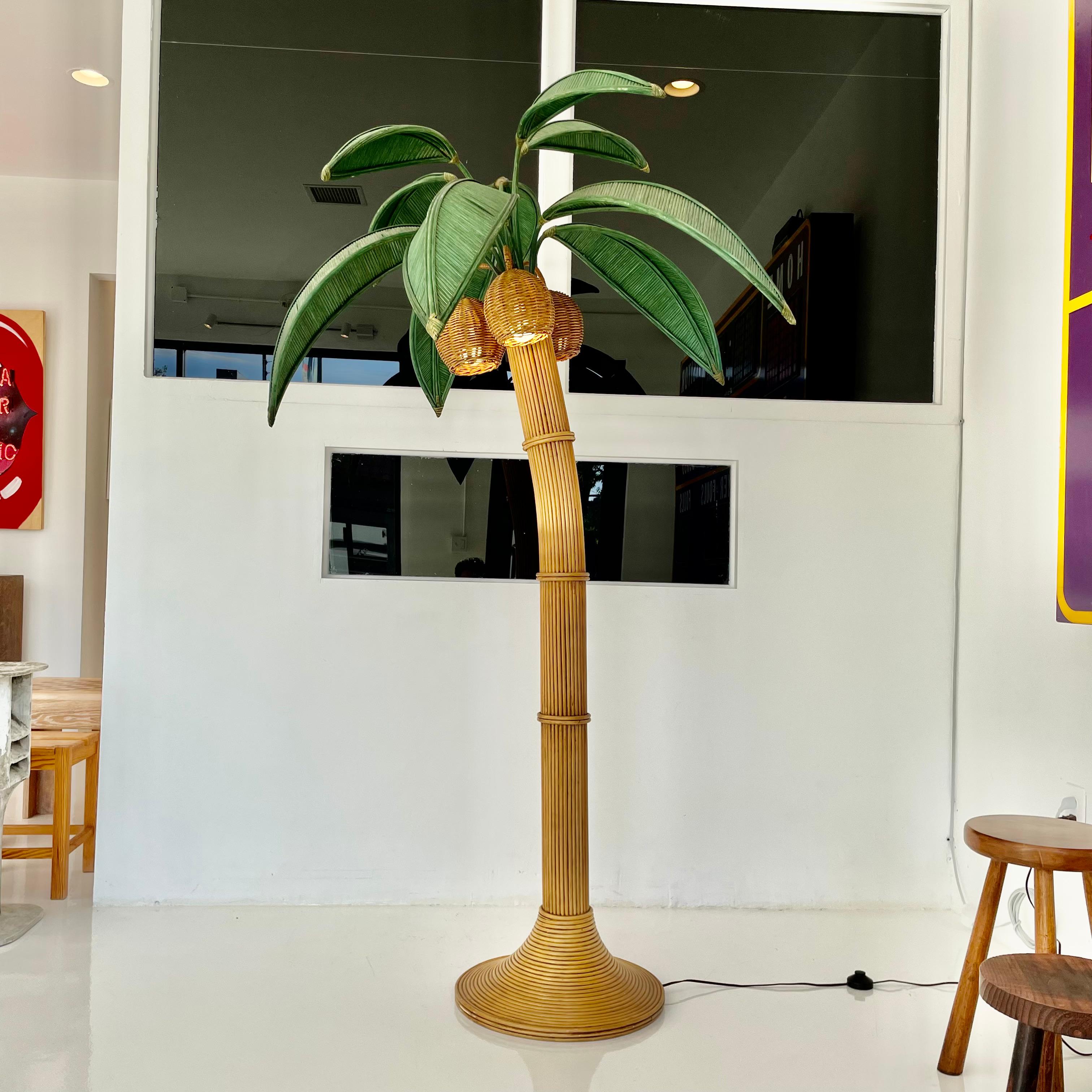 Beachy floor lamp of a Palm tree. Just under 7 feet tall. Made of rattan and wicker. Three wicker coconuts each contain a socket/light inside. Coconuts swivel. Green palm leaves made of wicker and rattan sprout out for the top. They rotate 180