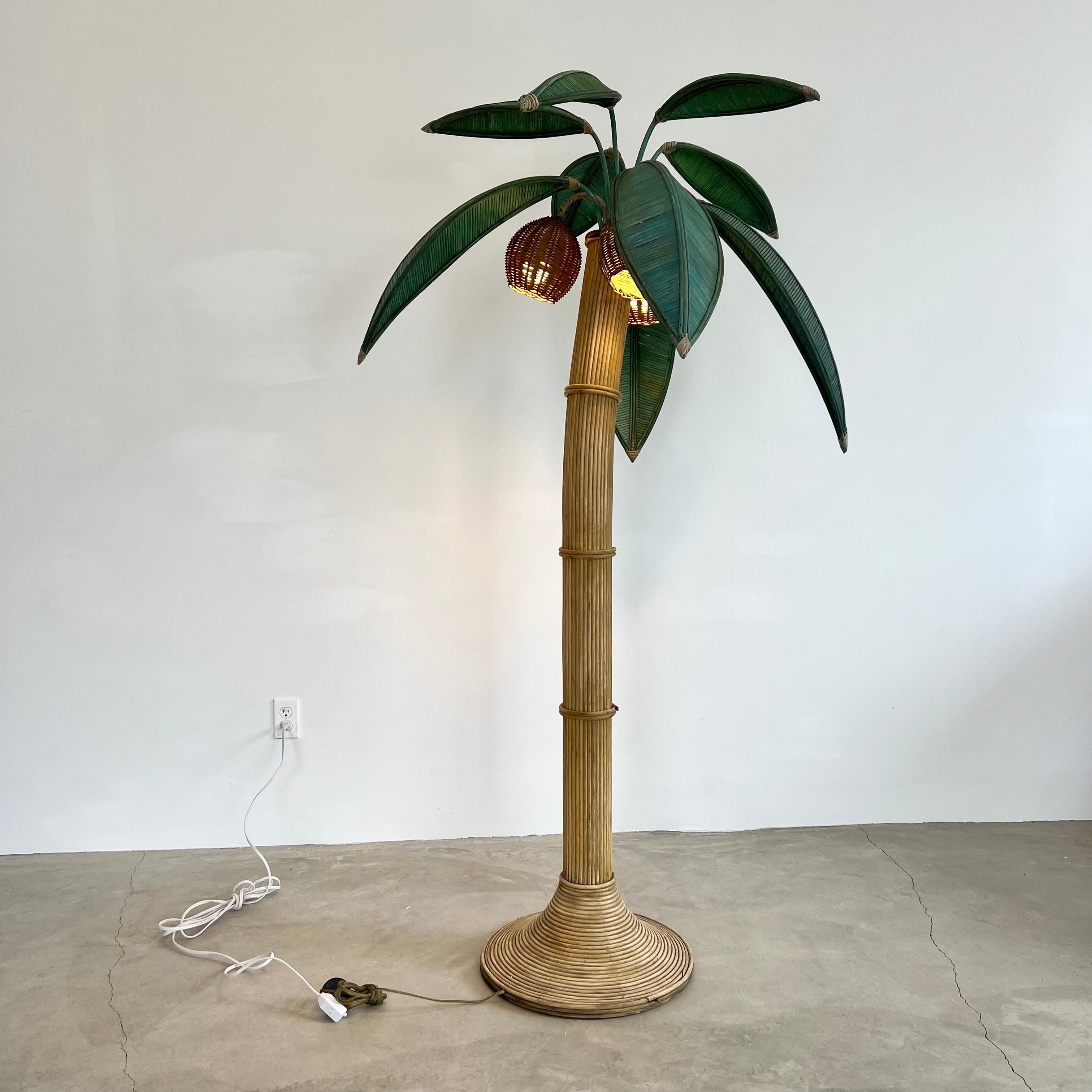 Beachy floor lamp of a palm tree. Original lamp made in the 1970s. Just under 7 feet tall. Made of rattan and wicker and bamboo. Curved trunk resembles a leaning palm tree. Three wicker coconuts each contain a socket/light inside. Coconuts swivel.