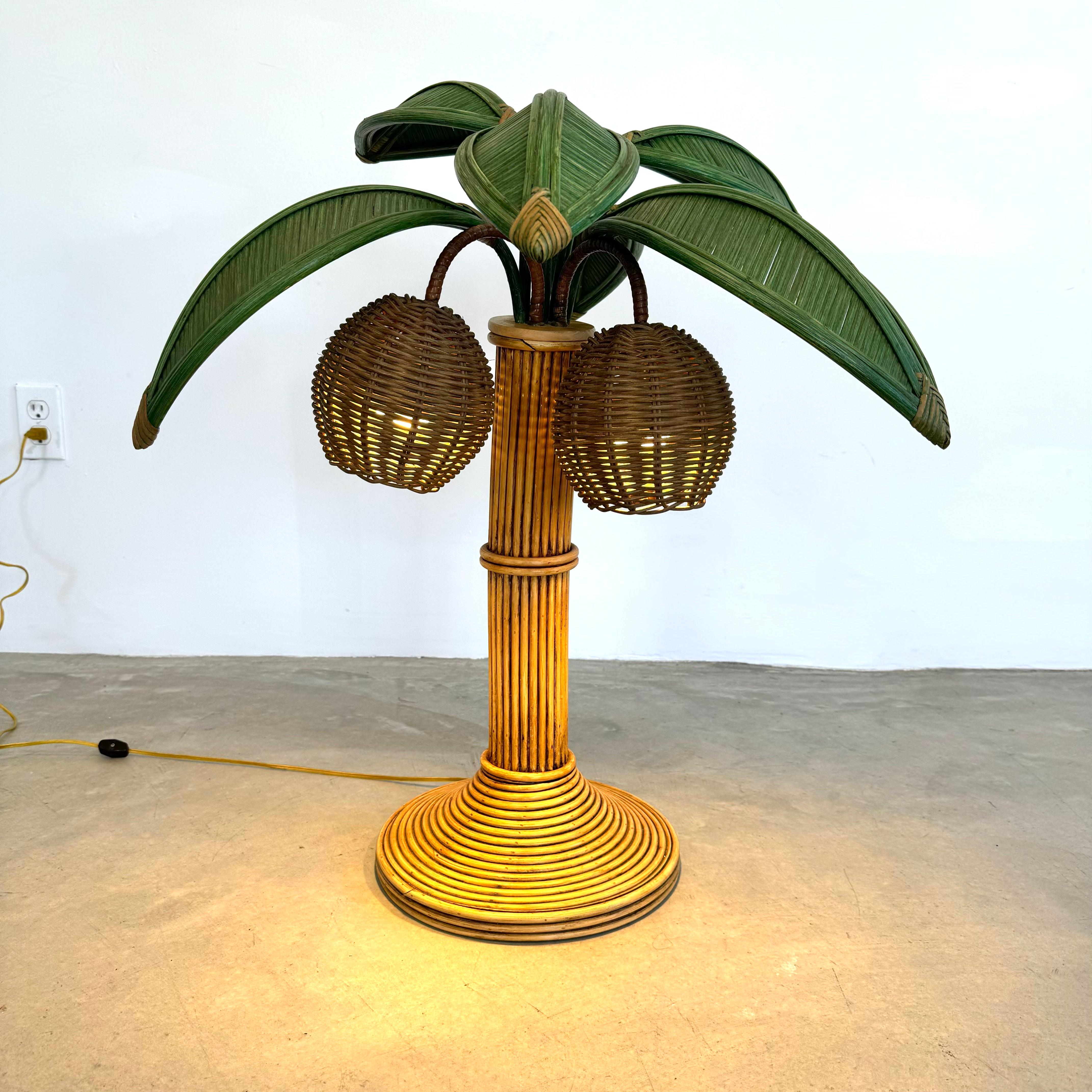 Beachy table lamp of a palm tree. Original lamp made in the 1970s. Made of rattan and wicker and bamboo. Curved trunk resembles a leaning palm tree. Two wicker coconuts each contain a socket/light inside. Six green palm leaves made of wicker and
