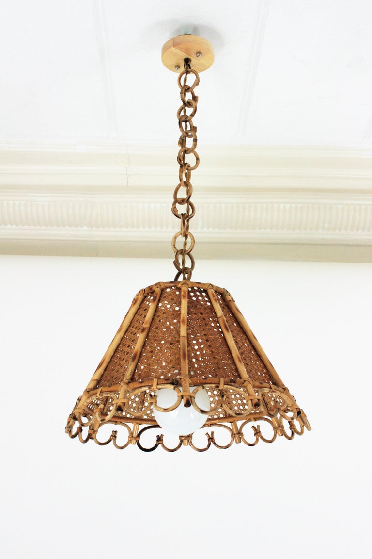 Mid-Century Modern woven wicker wire and rattan conical shaped lantern or pendant ceiling lamp. Italy, 1960s. 
The woven wicker shade of this lamp is accented by vertical rattan sticks and charming details at the bottom part. It hangs from a chain