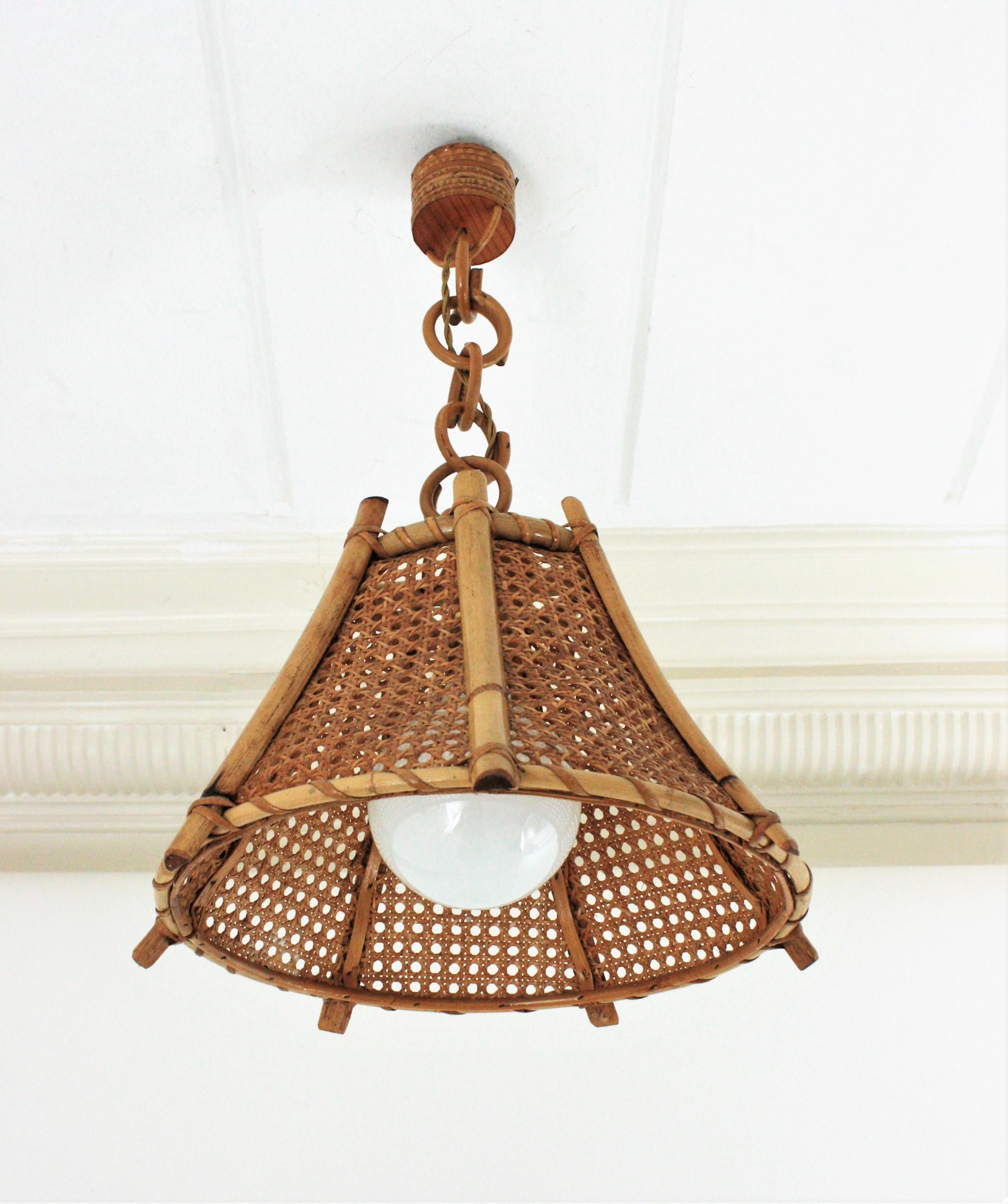 Bamboo Rattan and Wicker wire pagoda shaped pendant or chandelier, France, 1960s.
This midcentury suspension lamp features a wicker weave conical lampshade with bamboo vertical canes. It hangs from a chain with rattan links. We can add a larger