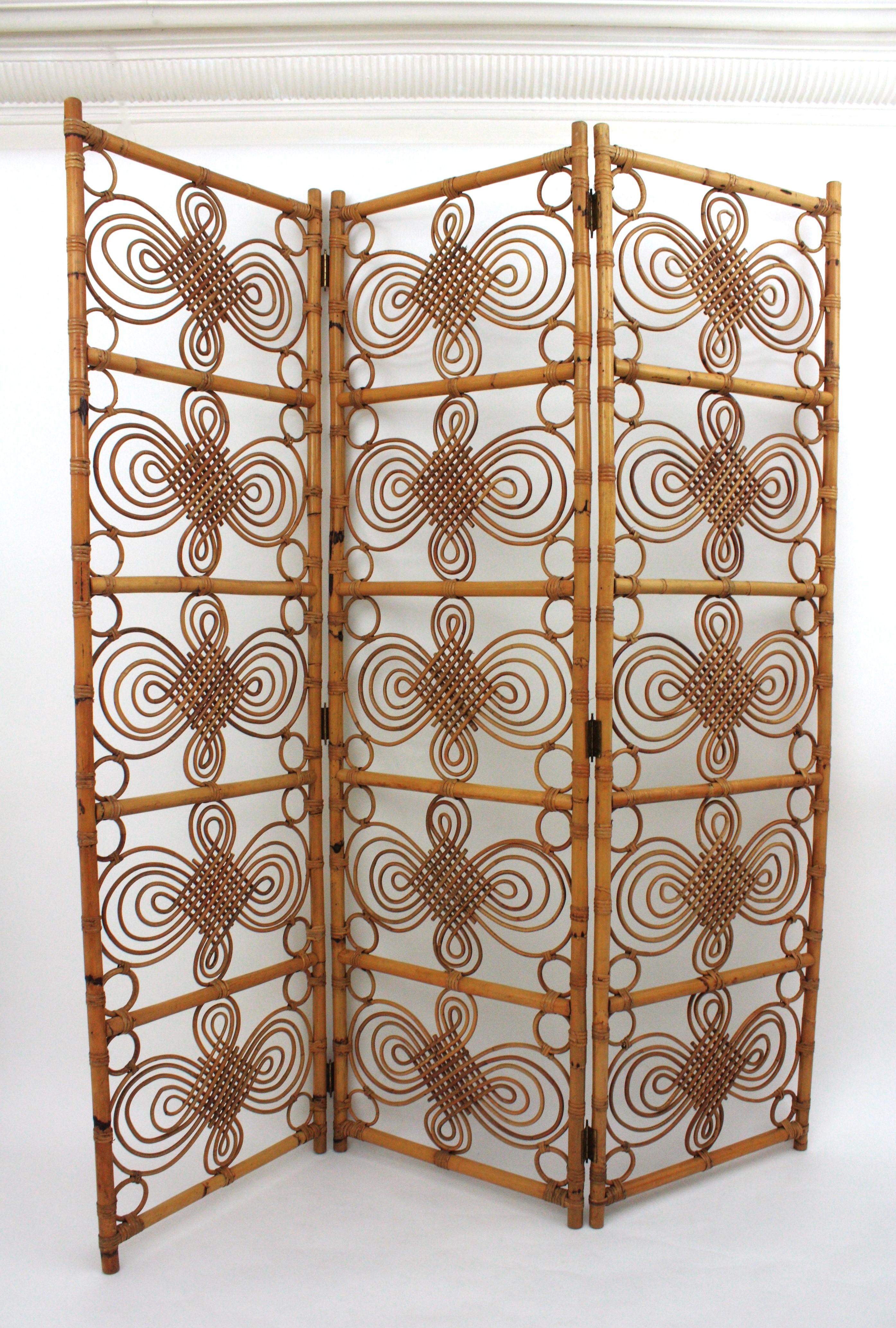 Eye-catching handcrafted rattan / wicker and bamboo three-panel folding screen / room divider with filigree decoration. Manufactured in Spain, 1960s.
This rattan folding screen combines Mid-Century Modern and chinoiserie accents.
It can be used as