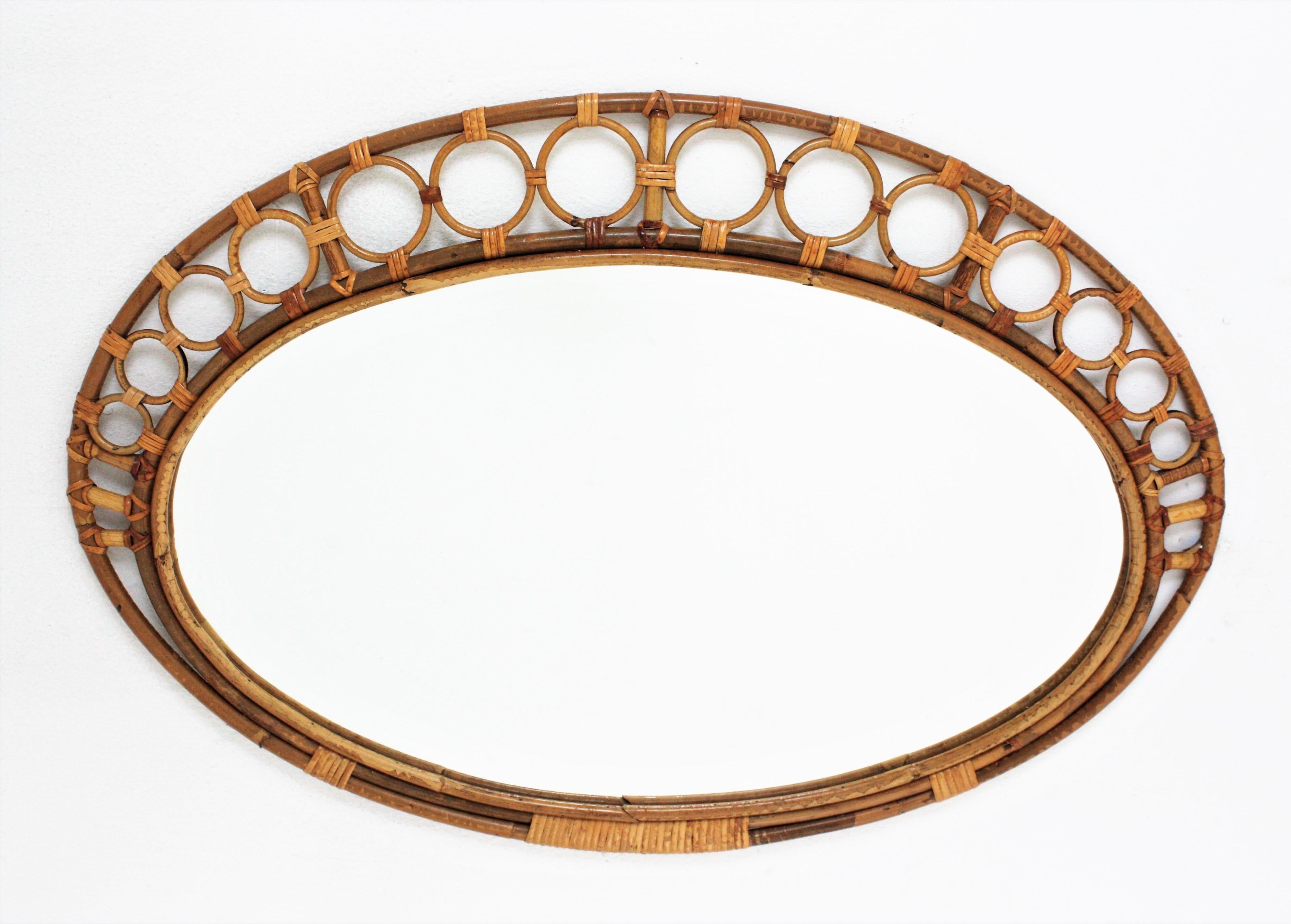 Auffälliger Mid-Century Modern Spiegel, handgefertigt aus Bambus und Rattan mit Ringen, die den Rahmen umgeben.
Dieser mediterrane Wandspiegel besteht aus einem ovalen Bambusrahmen, der von kreisförmigen Rattanverzierungen umgeben ist, die von der