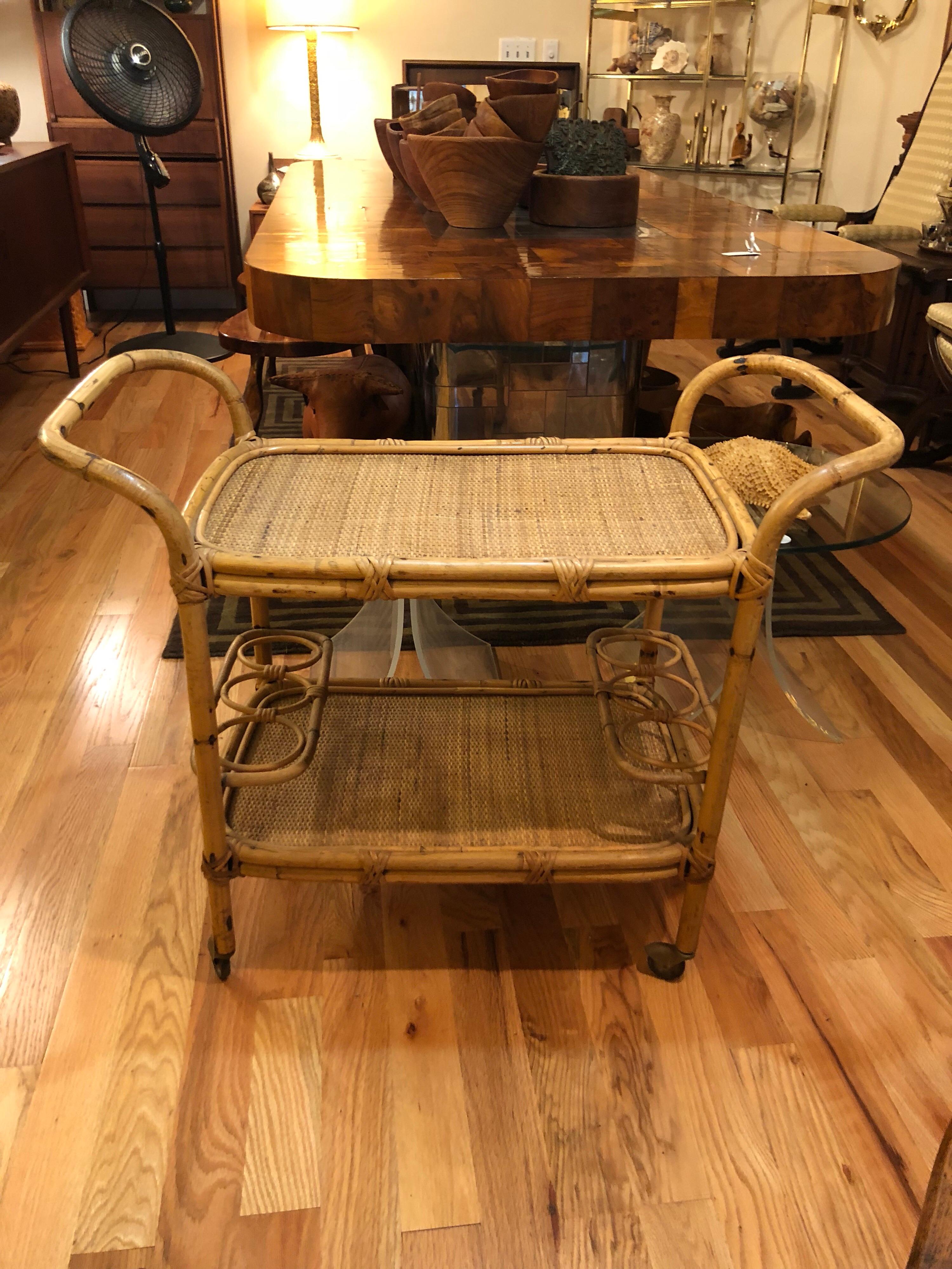 Rattan bar cart on casters. This two-tiered piece is perfect for entertaining. The bottom of which holds 6 bottles. Nice tropical feel in this design . Wicker weaved tops and bamboo style handles. Perfect for a poolside party or beach cabana.