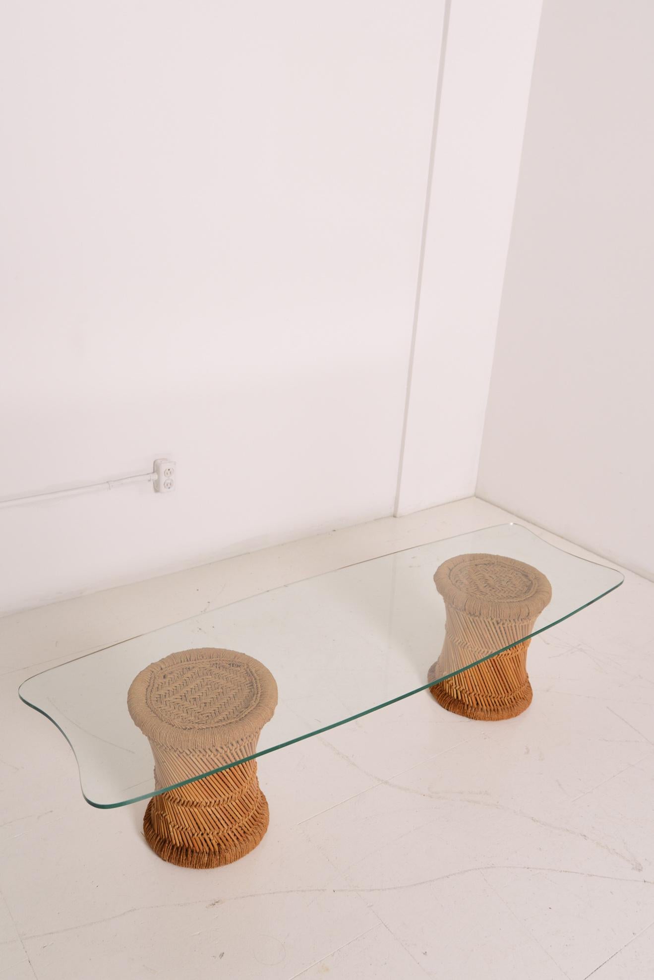 Rattan base glass top coffee table. Two rattan pedestals show off all their flavor through the glass top. Nothing too sharp or straight here, the tabletop edges and ends curve in and out, concave and convex, to match the round design of the two