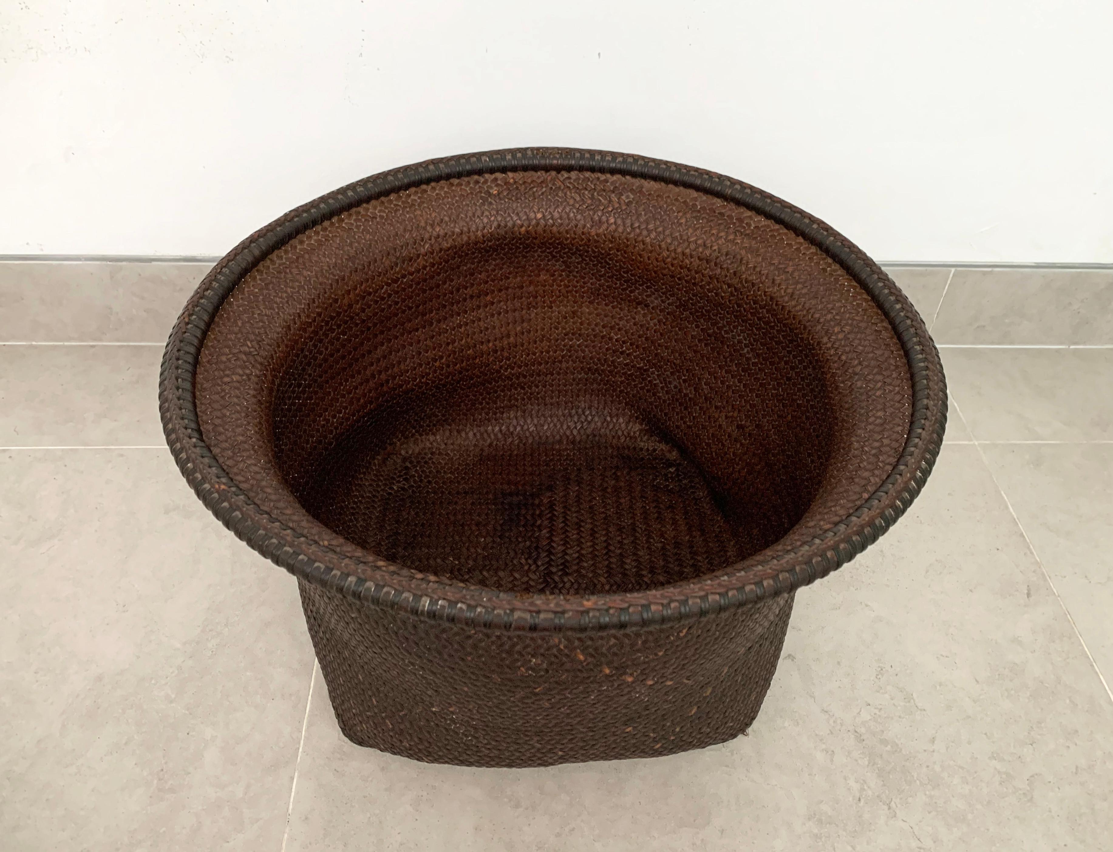 This mid-20th century hand-woven basket originates from the Dayak tribe of Borneo, crafted with rattan fibres. These baskets were used to carry leaves, fruit, grain and wood and features wonderfully aged fibres and wood patina. This basket has a