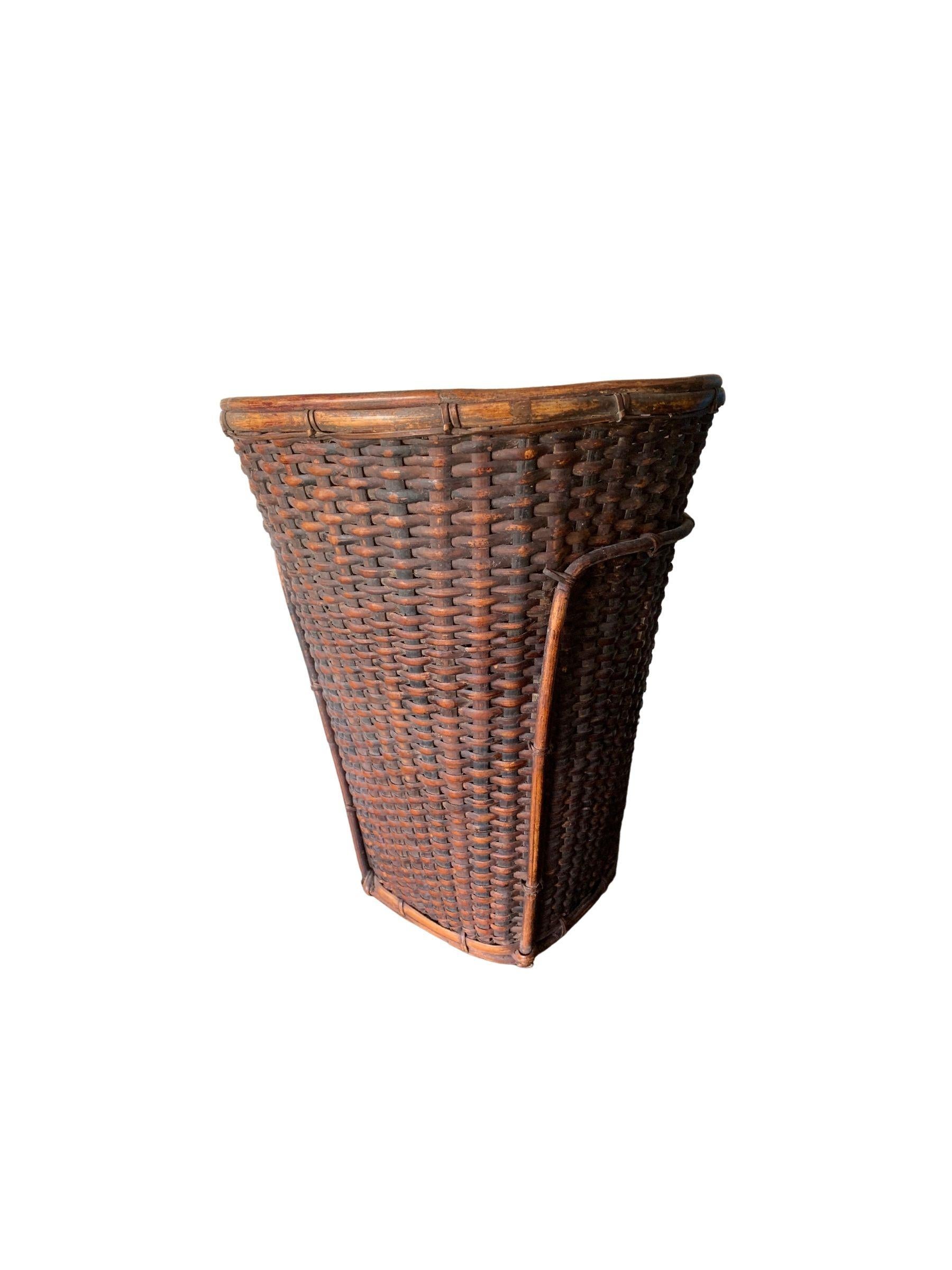 This mid-20th century hand-woven basket originates from the Dayak tribe of Borneo crafted with rattan fibres. These baskets were used to carry leaves, fruit, grain and wood and features wonderfully aged fibres and wood patina. The various weaving