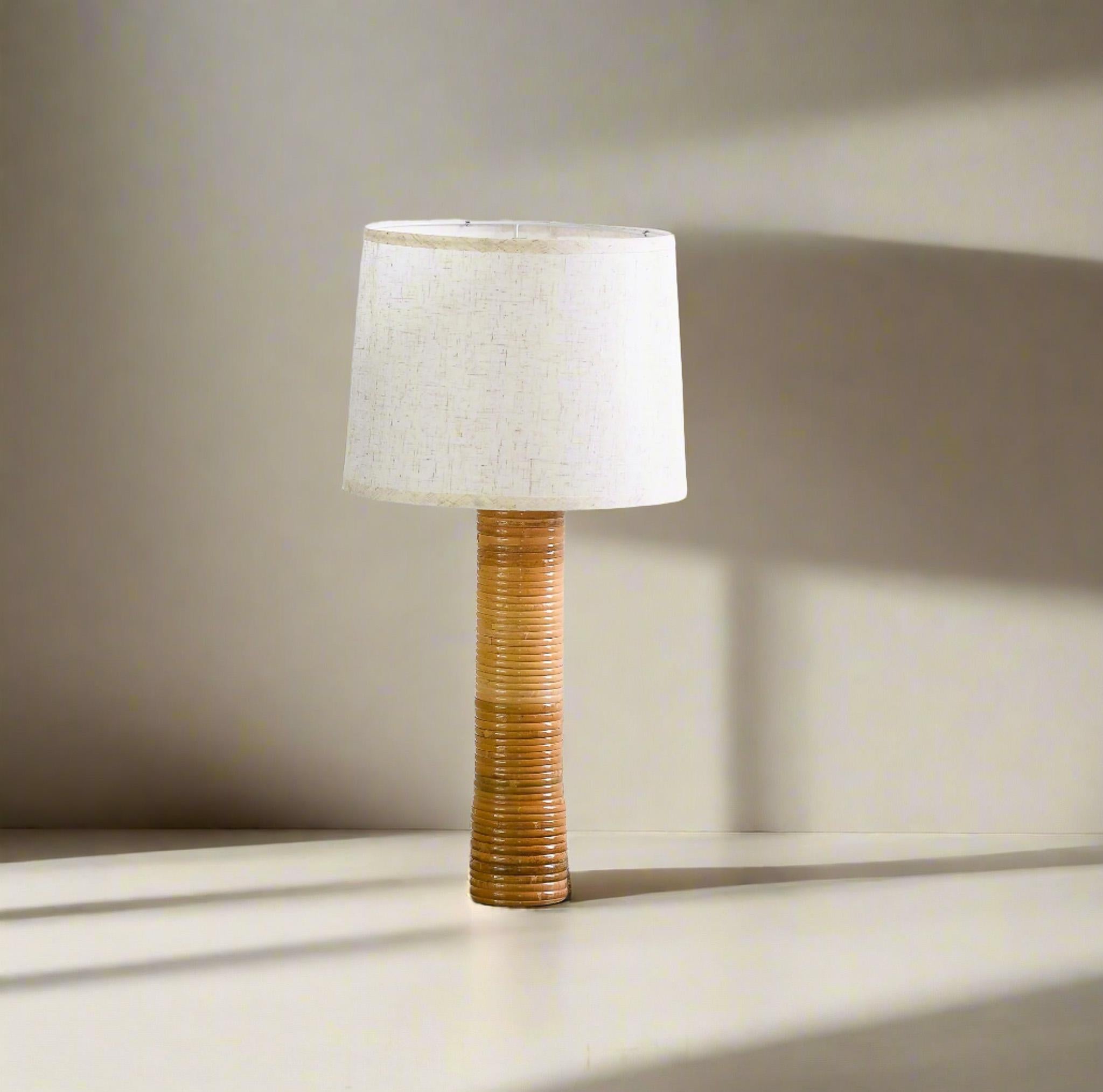 Add sophistication to your room with this Artisanal Mid Century Modern Style Rattan Wrap Table Lamp. The cane-wrapped vertical base brings a distinct texture and cozy feeling to any space. The lamp's natural rattan hues create a luxurious and