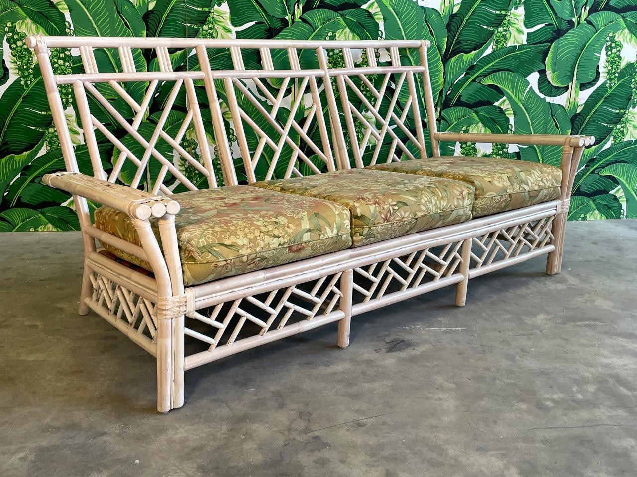 Rattan sofa features fretwork in the Chinese Chippendale style, perfect to complete your chinoiserie look. Includes seat and back cushions in very good condition, fabric slightly dated and could use reupholstering. Frame in very good condition with