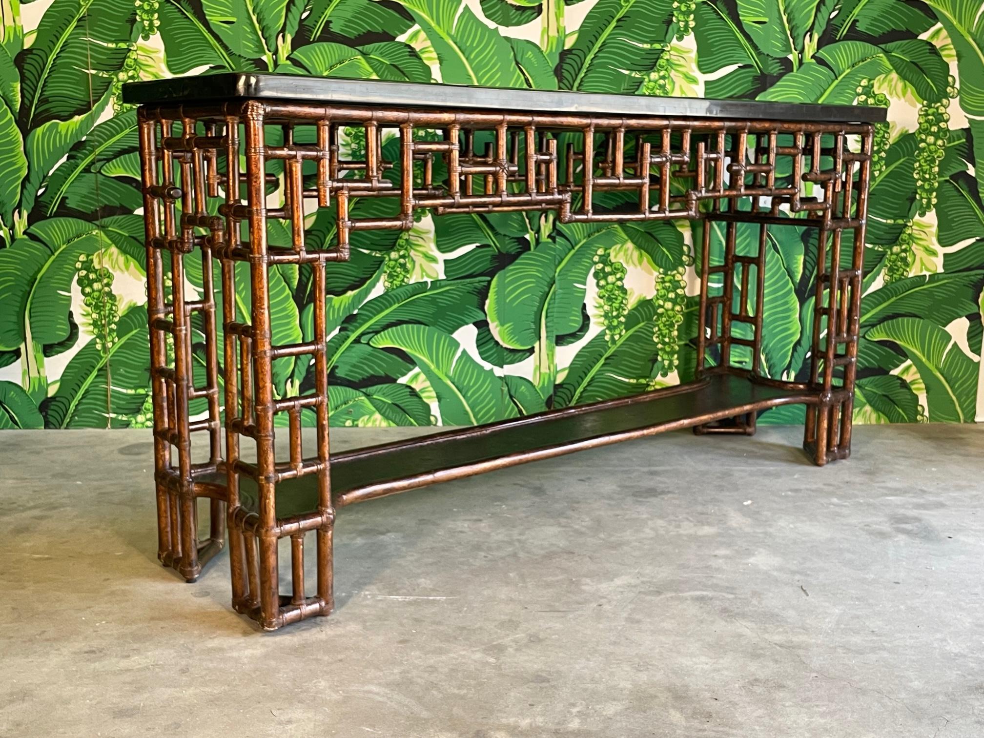 Burnt rattan/bamboo console table features a tessellated marble top with beveled edges and decorative inlay, and a deep, rich finish to the leather-wrapped frame. Chinese chippendale fretwork is mirrored on front and back. Good condition with