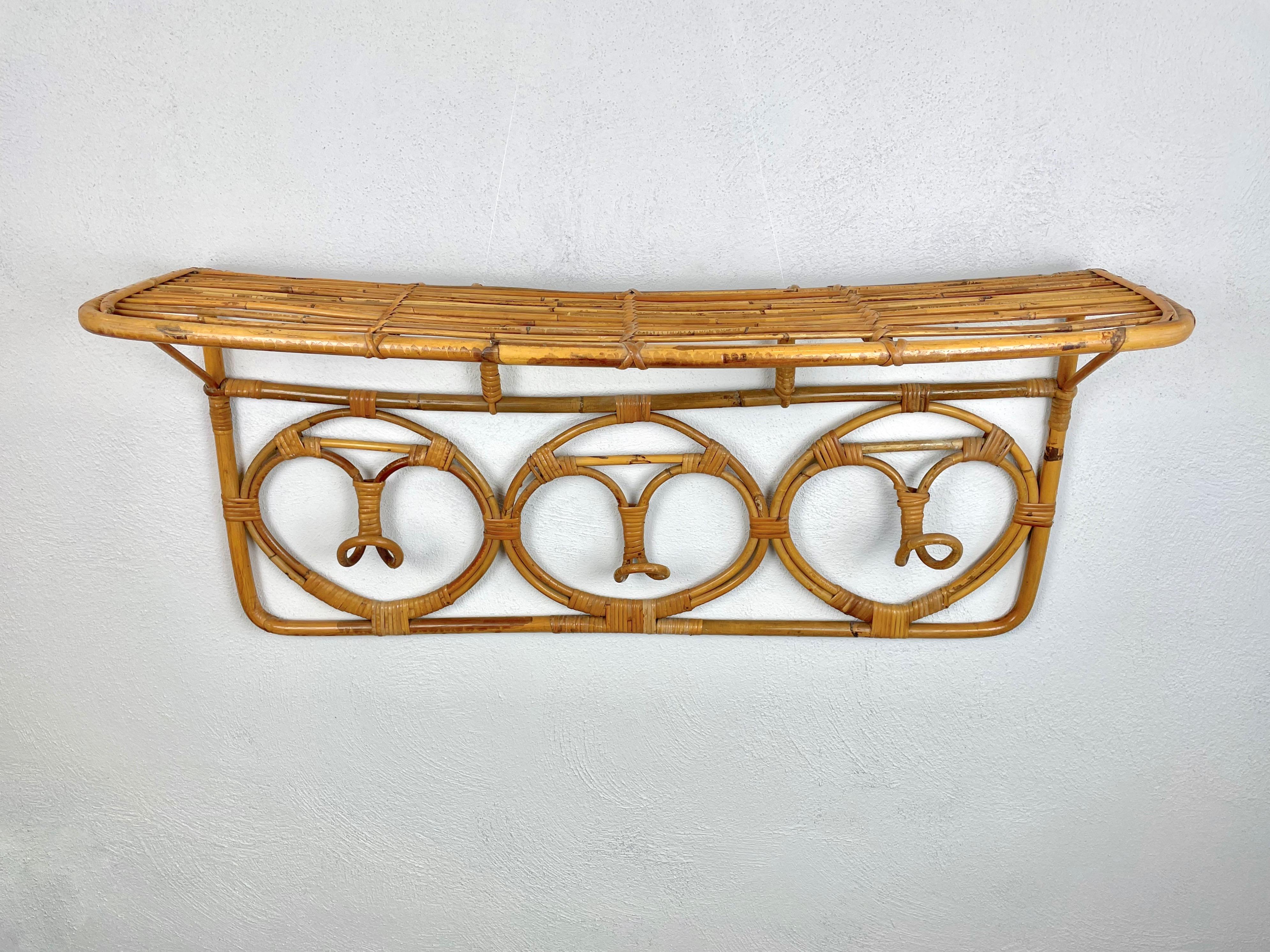 This coat hanger was produced in Italy in the 1960s and features three hooks for hanging clothes and a shelf for objects/bags, everything in rattan.