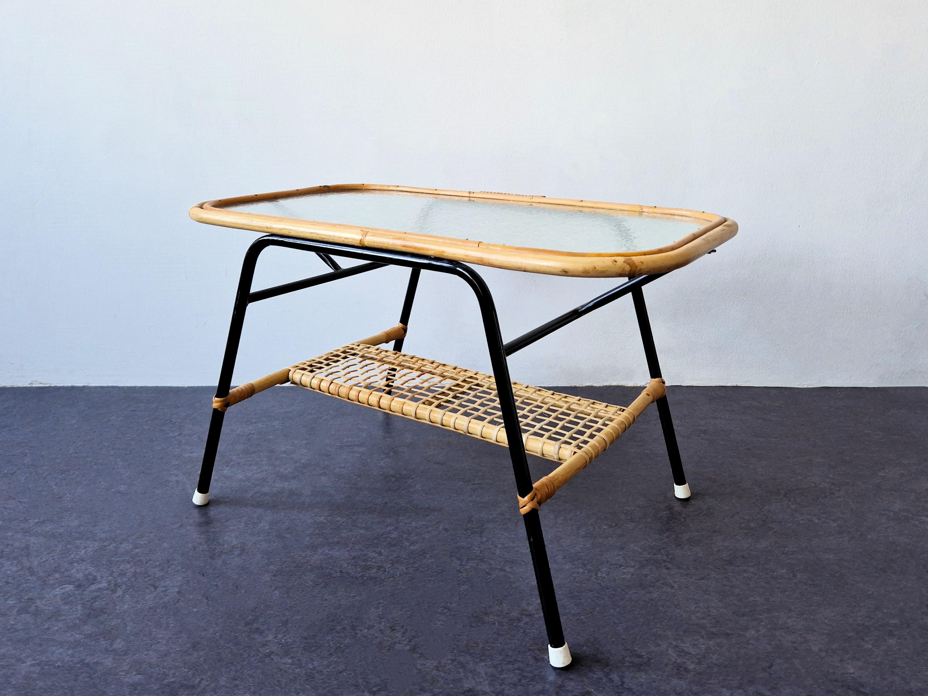 This coffee table was designed for Rohé Noordwolde in The Netherlands in the 1950's. The table has a black lacquered metal base with a rectangular rattan and cloud glass table top. The black laquered frame gives a nice contrast to the rattan. It has