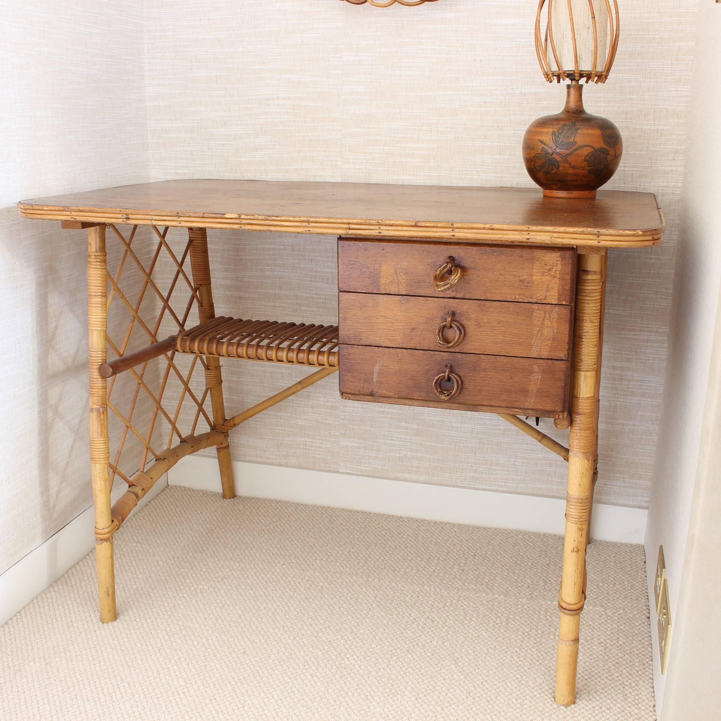 Rattan desk or vanity table by Louis Sognot, circa 1950s. Characteristic of its period, there are three drawers located under this rattan desk as well as a storage shelf. Rattan grilled panels connect the side legs. The desktop is edged with rattan