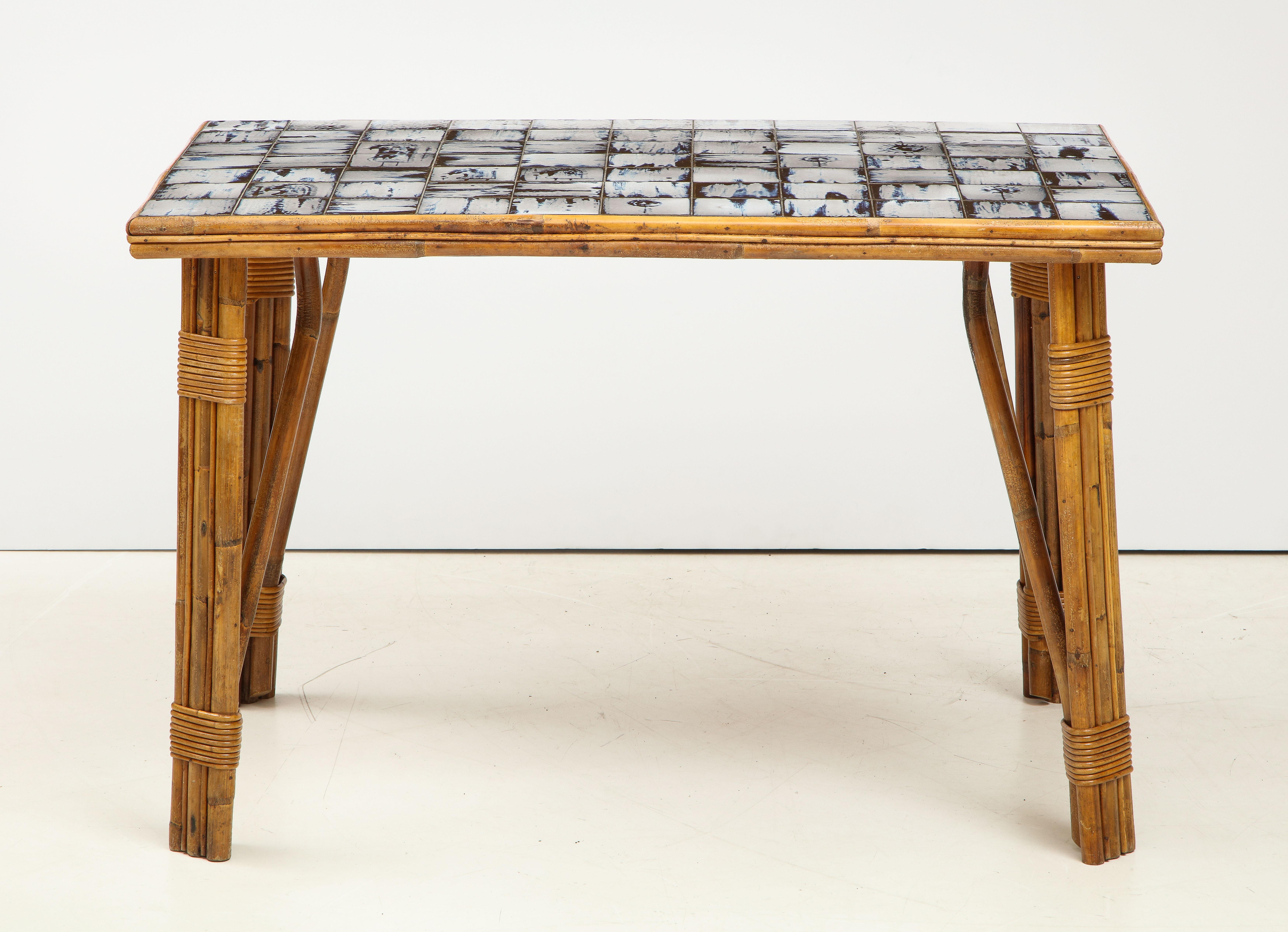 Mid-century rattan dining table with a stunning hand-painted ceramic tile top, France, c. 1950s.

Table consists of rattan-wrapped legs, a tripart edge, and an inlaid ceramic tile top with a gorgeous blue and white painterly design.