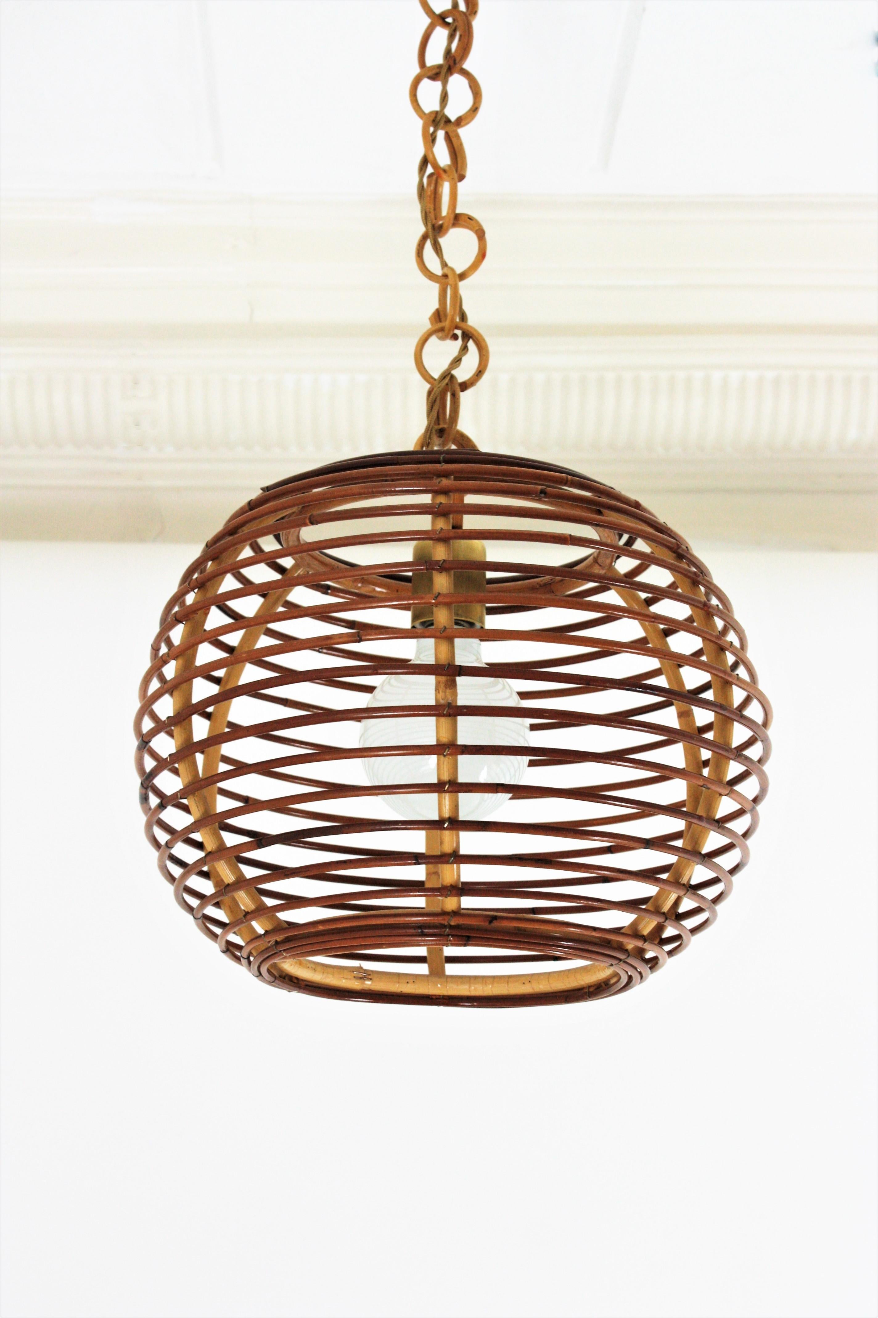 Spanish Modern rattan lantern with globe or ball shaped lampshade, Spain, 1950-1960s.
This suspension lamp is entirely handcrafted with rattan. The ball shaped shade hangs from a chain with round rattan links topped by a rattan canopy. The chain