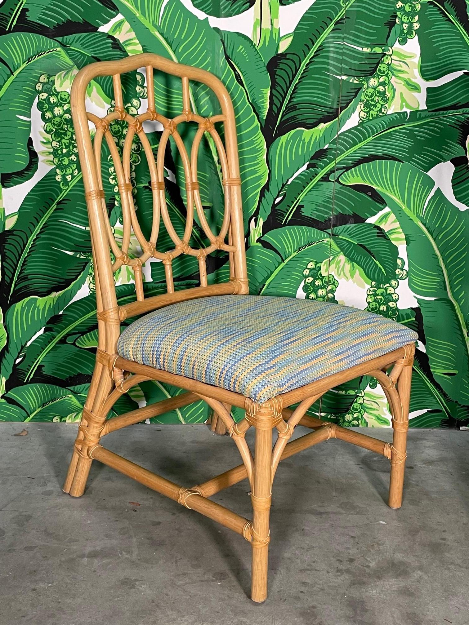 Set of six McGuire style rattan dining chairs feature an organic loop back design and leather wrapped joints. Decorative spandrels and splayed rear legs complete the well-constructed frame. Good condition with only minor imperfections consistent