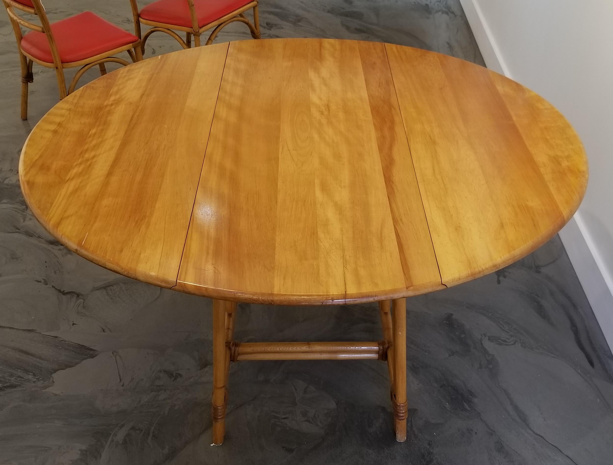 A circular gateleg dining table by Heywood Wakefield. Beautiful wood grain to solid maple top with warm glow to finish. Steamed ash hardwood undercarriage bound with rattan. Fully open measures 54 inch diameter. Retains Heywood Wakefield branded