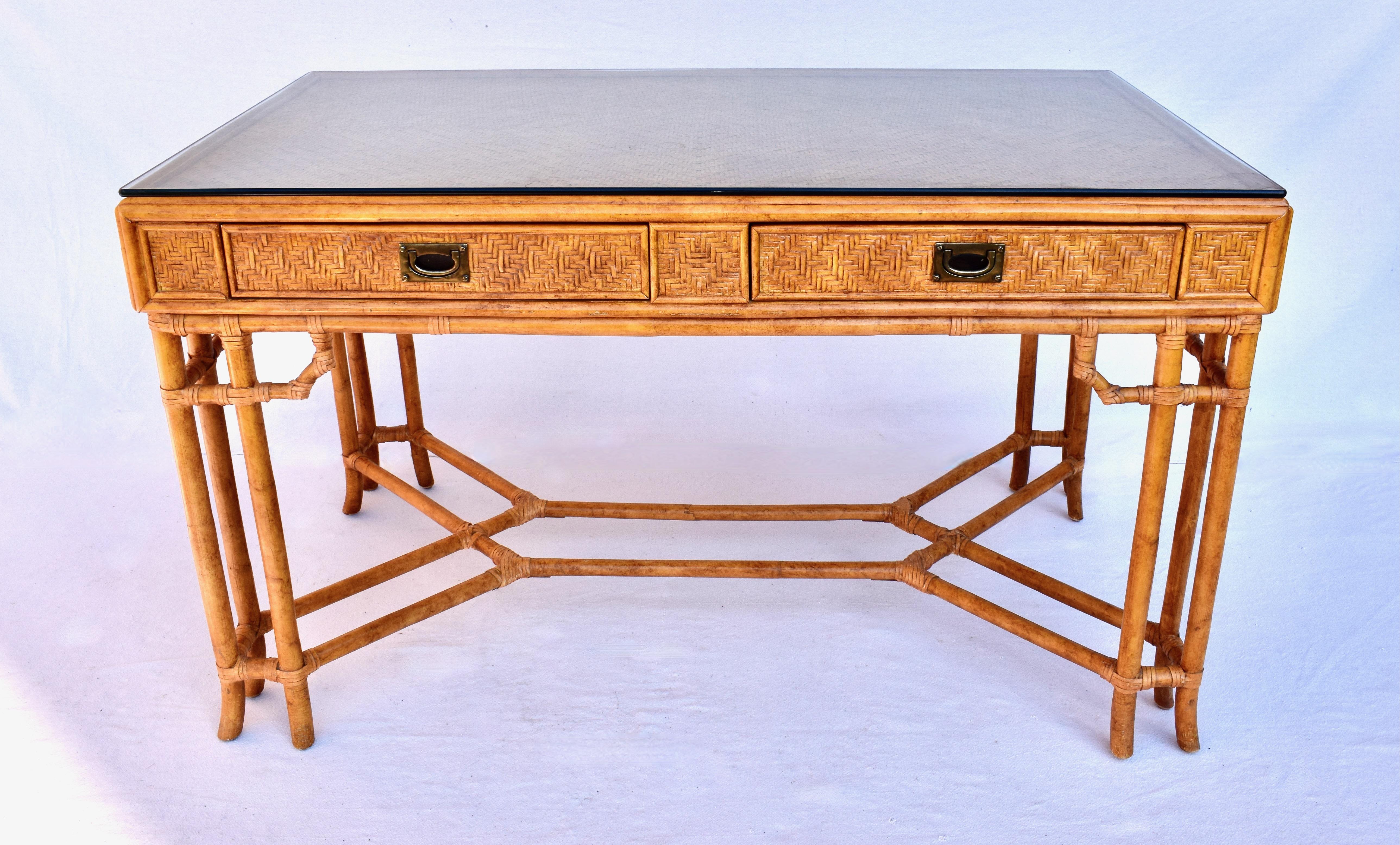 Midcentury British colonial campaign style 2-drawer writing desk or work table with distinct Chinese Chippendale design elements. Bamboo frame construction wrapped in woven cane rattan grass cloth & rawhide leather joinery features generous work