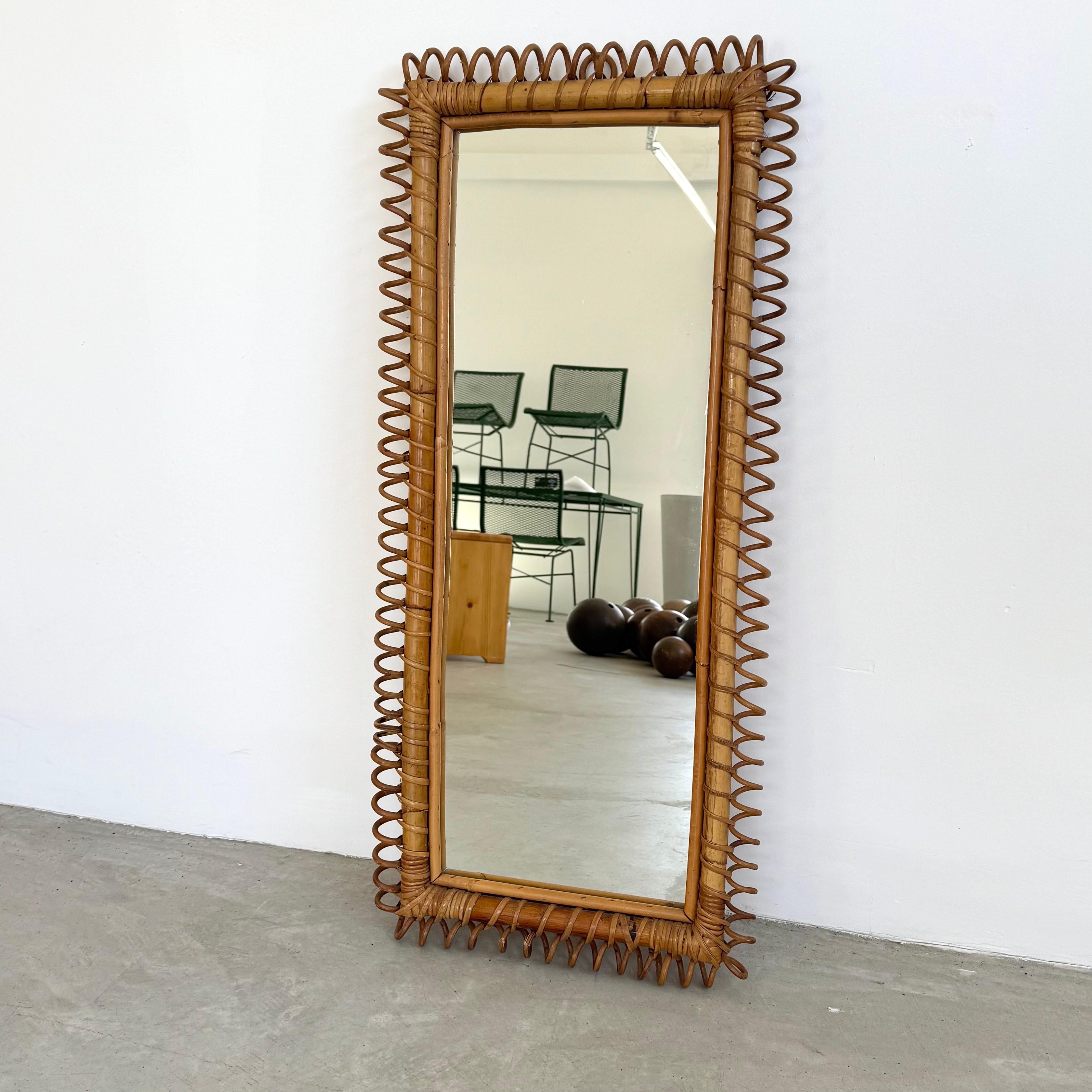Ce miroir éclectique en rotin constitue un bel accent fantaisiste. Le miroir rectangulaire est orné de rotin ondulant, méticuleusement tressé. Suspendu à une fixation au dos, il semble flotter sans effort. Robuste et de bonne facture. En bon état