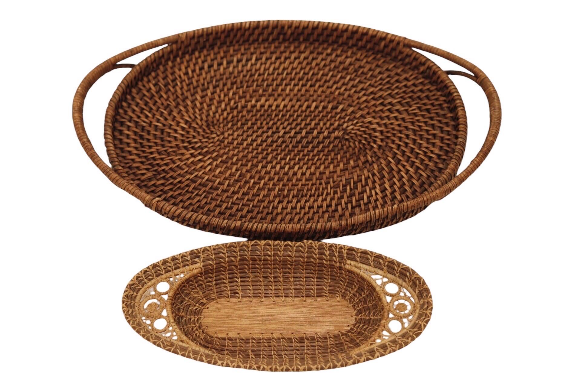 A set of two oval serving trays. The smaller is an antique pine needle tray, hand woven and decorated with hand knotted “sun” medallions at each end. The larger tray is a hand woven rattan, with rattan handles. Trays measure 21