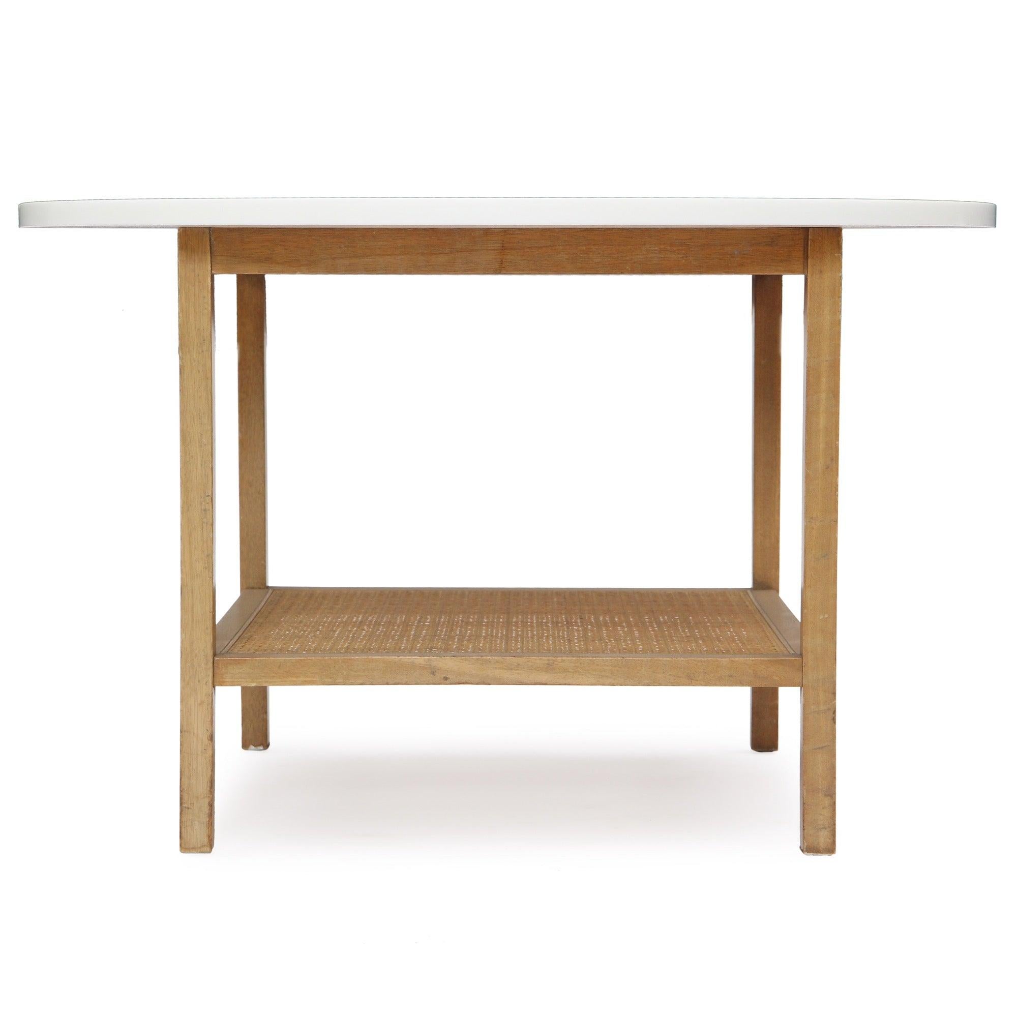 A end / side table constructed in light walnut wood with a round top of opaque Vitrolite glass and features a rattan lower shelf.