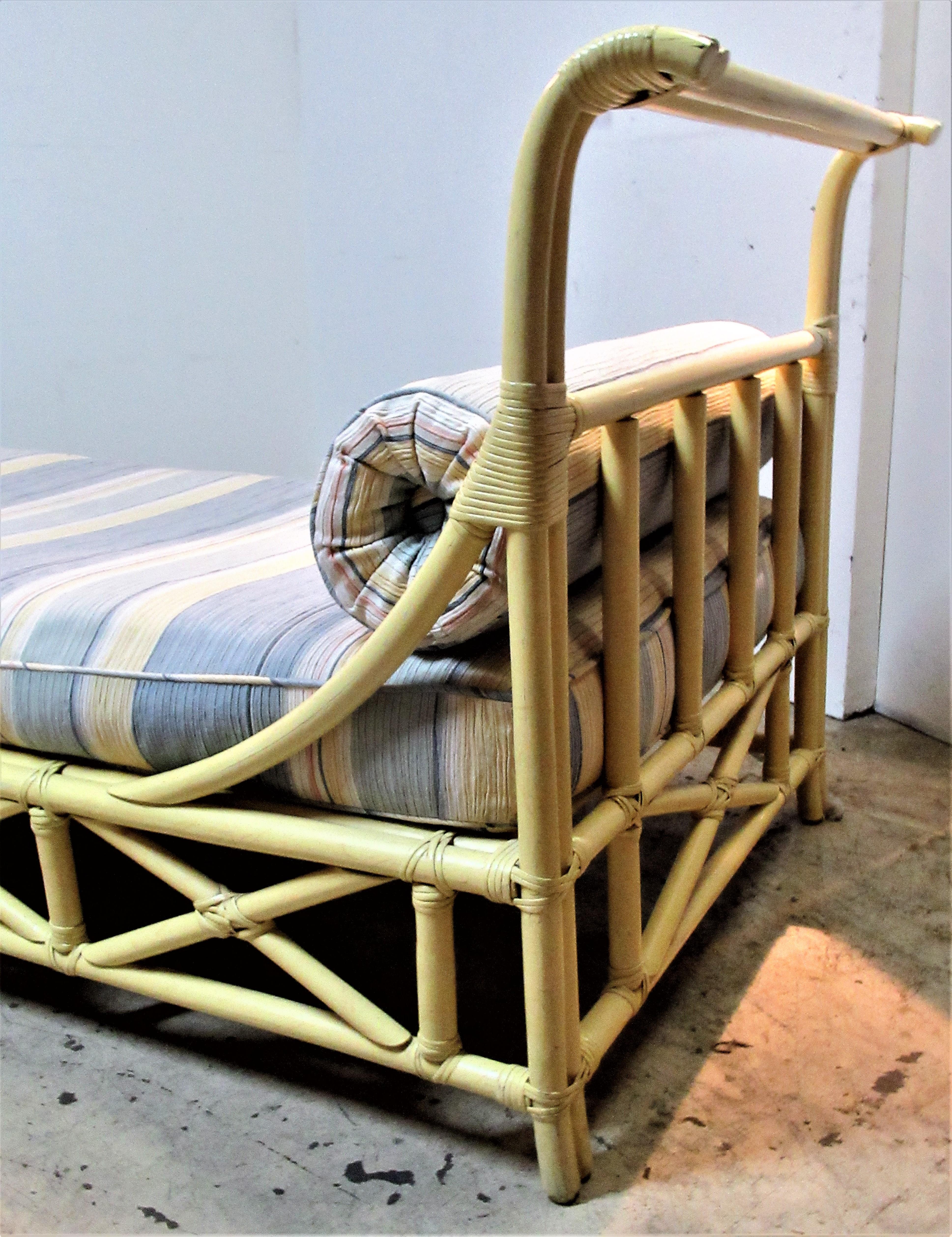 Old soft yellow painted rattan daybed lounge by Ficks Reed (see picture 10 of Ficks Reed silver foil label and picture 9 of original straps) with beautifully upholstered striped ribbed cotton long seat and bolster cushions. Great form, circa 1960.