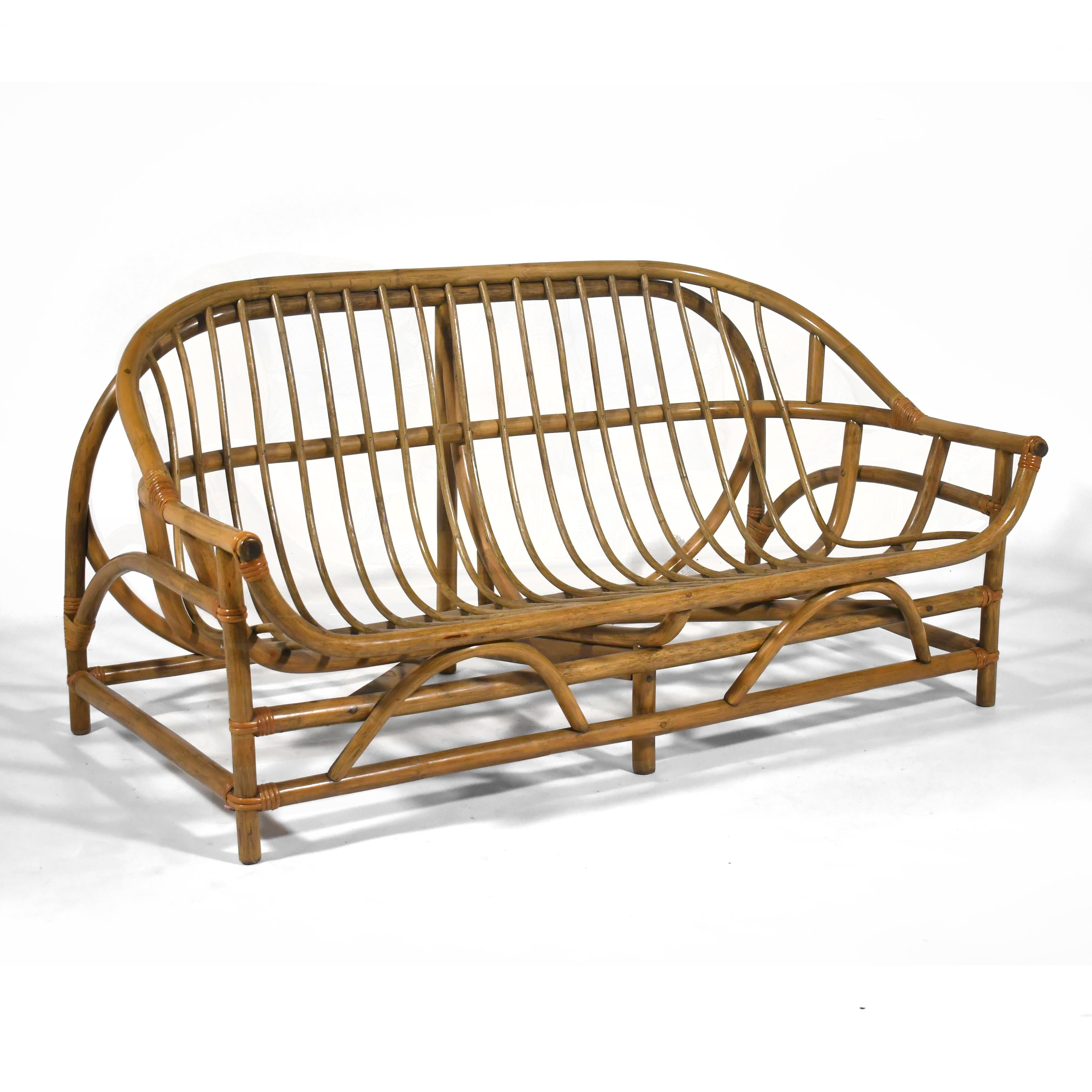 Ce charmant canapé en rotin présente un cadre dynamique aux lignes courbes et évasées qui en font un plaisir sous tous les angles. La forme en panier berce les coussins de l'assise et du dossier et permet une assise très confortable. Bien qu'il ne