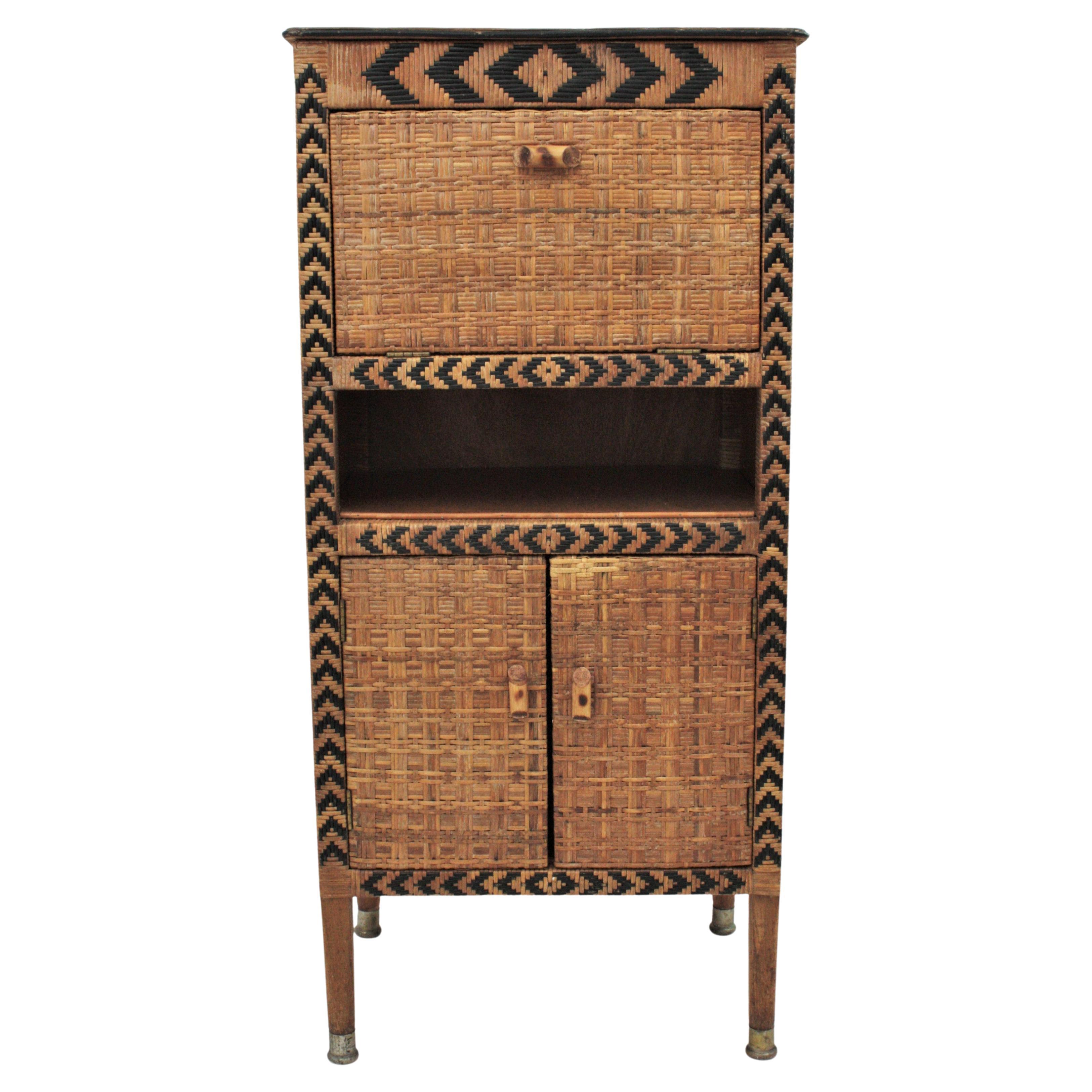 Eye-catching Rattan Victorian Style Tall Cabinet. France, 1940s.
This rattan cabinet features a wooden structure upholstered with woven rattan in two tones. It has three doors and one shelf and a black pattern decorating the front part.
It has an
