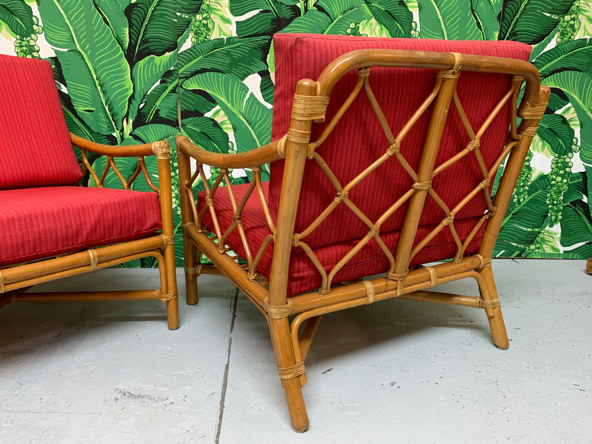 Pair of rattan lounge chairs feature leather wrapped joints and cross-hatch rattan detailing. Cushions are upholstered in an indoor/outdoor fabric. Very good vintage condition, minor imperfections consistent with age, some slight discolorations on