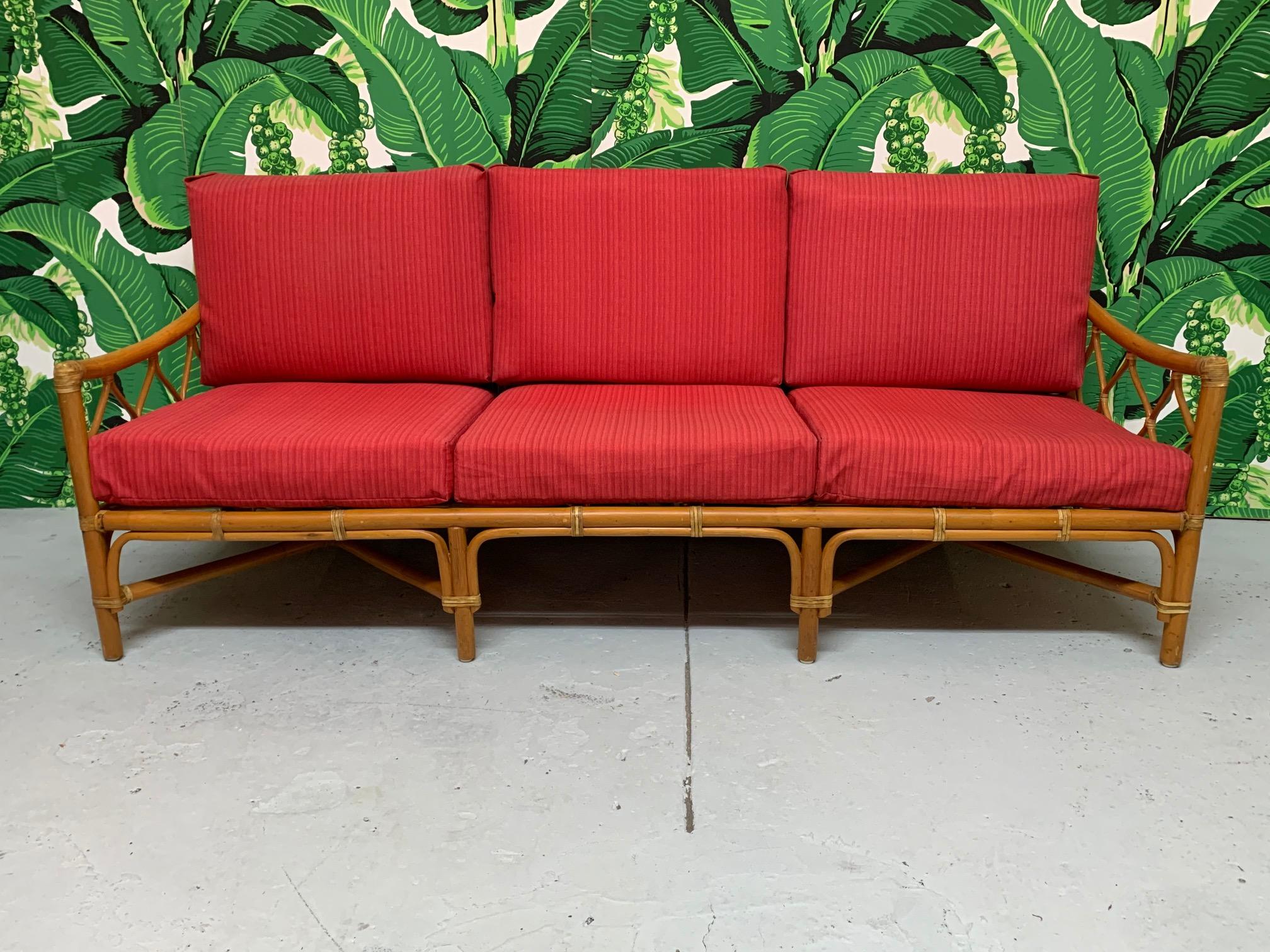 Rattan sofa features leather wrapped joints and cross-hatch rattan detailing. Cushions are upholstered in an indoor/outdoor fabric. Very good vintage condition, minor imperfections consistent with age, some slight discolorations on cushions.