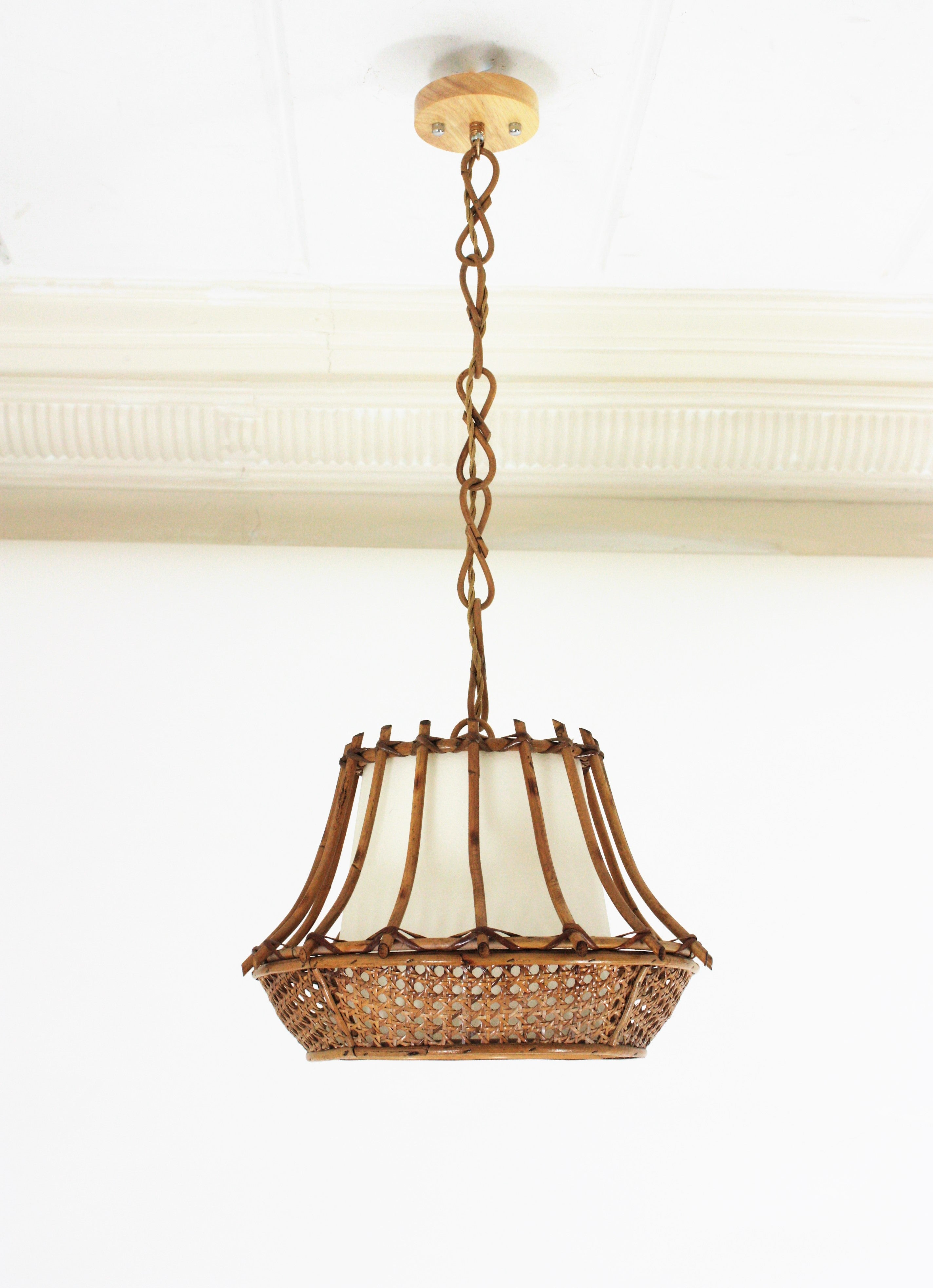 Rattan and Wicker wire pagoda shaped pendant or chandelier, France, 1960s.
This midcentury suspension lamp features a wicker weave conical lampshade with rattan vertical canes and and interior paper lampshade to difusse the light. It hangs from a