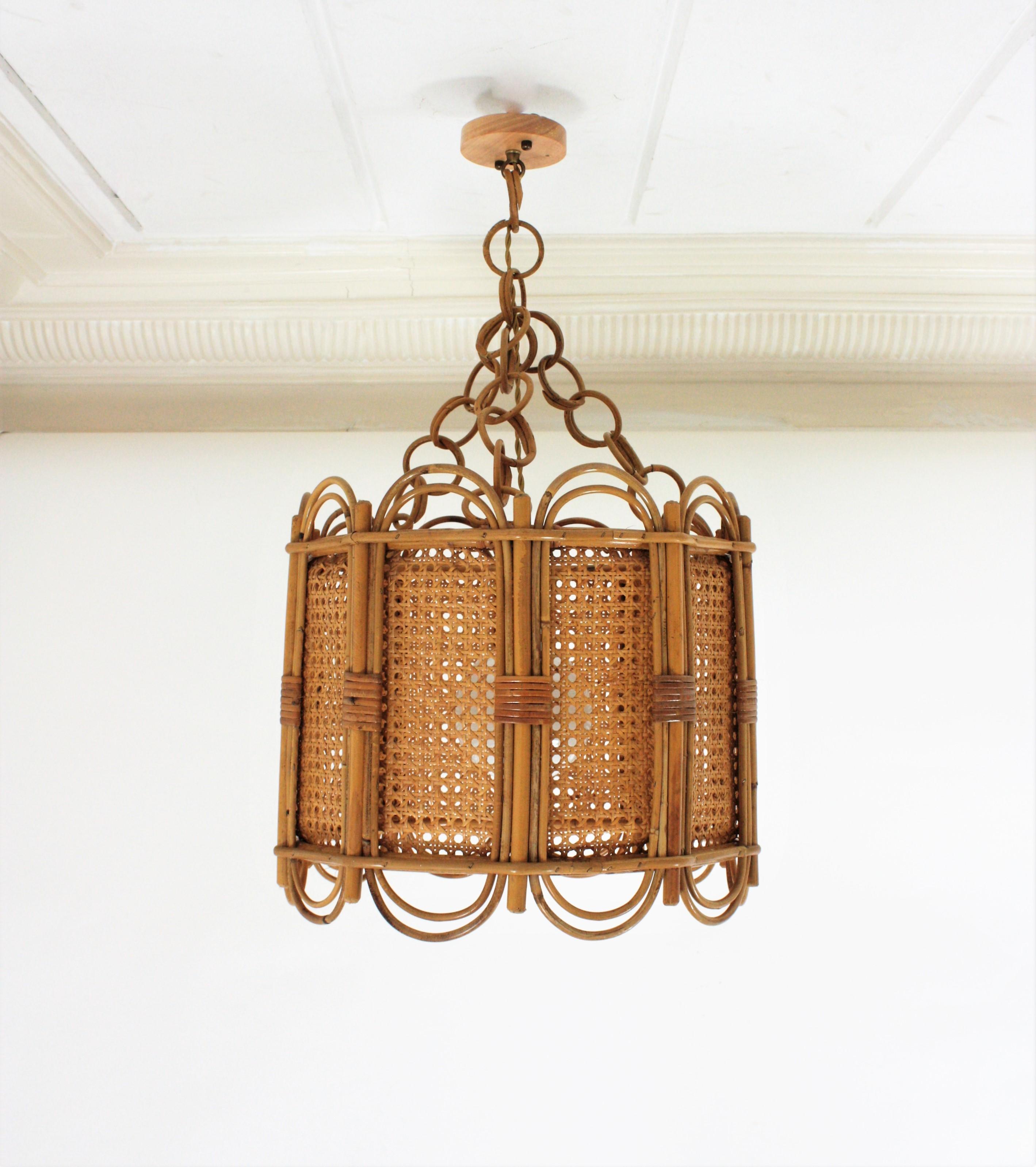 Spanish 1960s Mid-Century Modern rattan and wicker wire pendant lamp or lantern.
This eye-catching suspension lamp features a rattan drum shaped structure with wavy top an bottom and woven wicker panels.
It hangs from a triple chain with rattan