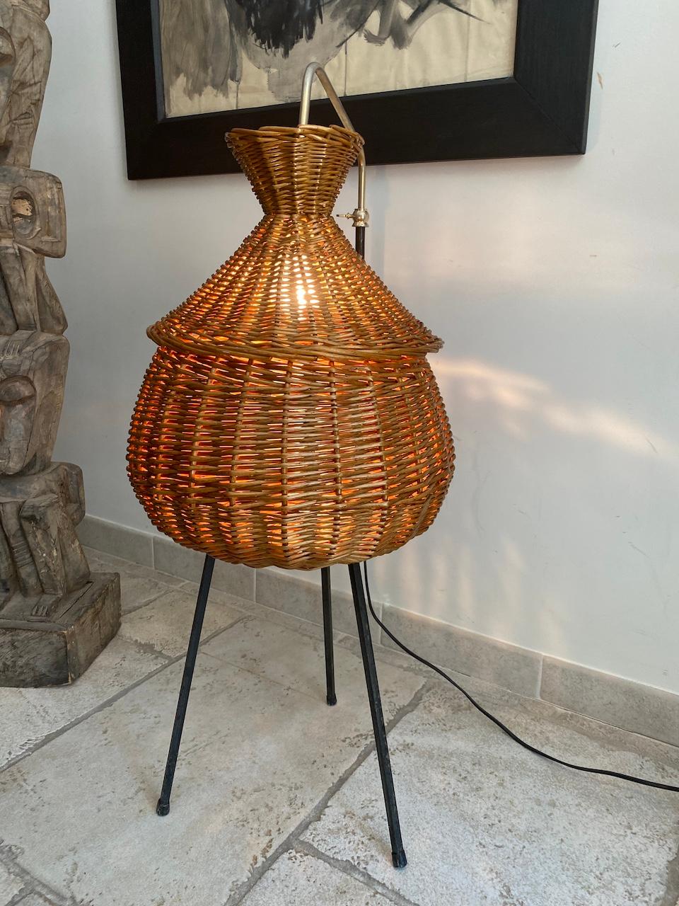 Floor lamp in the shape of an open or closed worker in rattan. It slides on a brass rod and can have several heights or positions. Wrought iron tripod base.