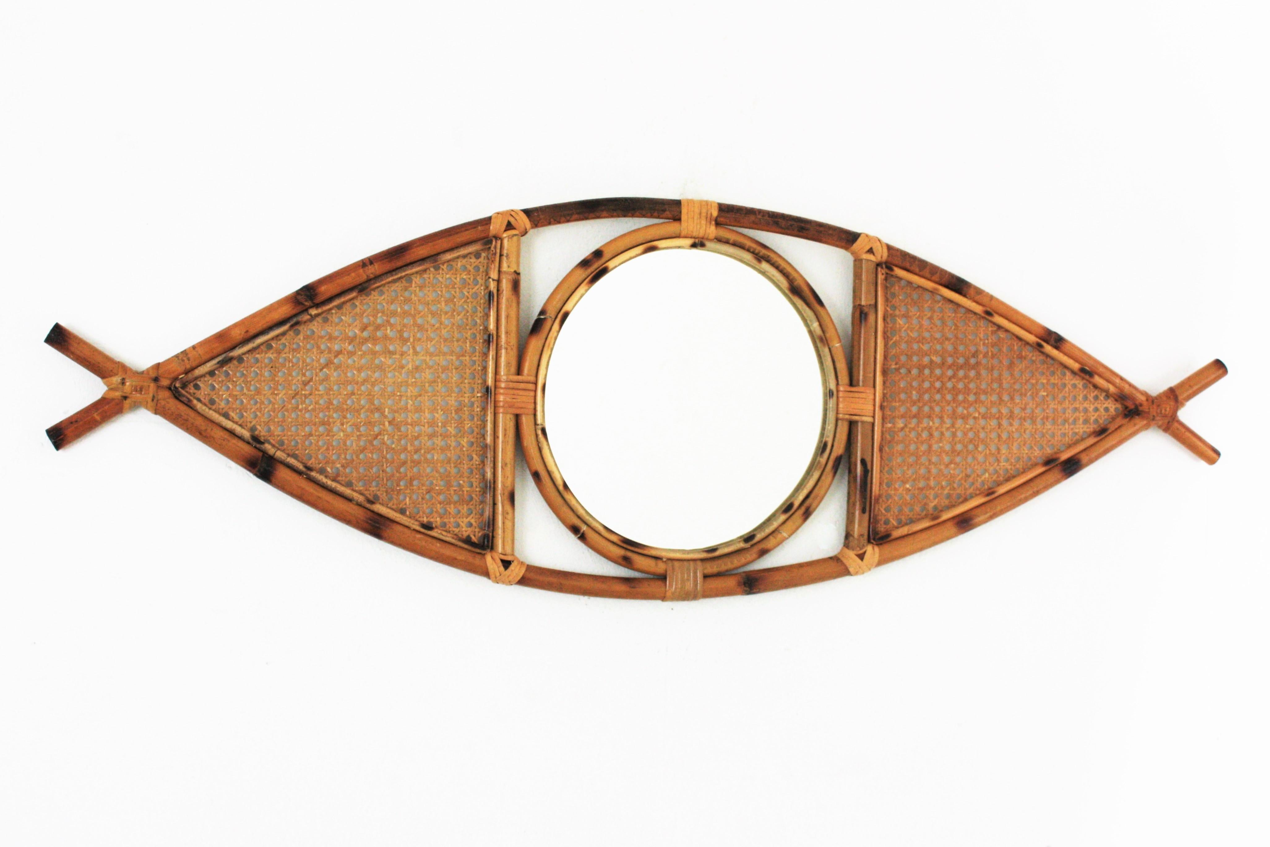 French Riviera Bamboo and rattan eye shaped mirror. France, 1960s.
This cool mediterranean mirror features a rattan / bamboo structure with the shape of an eye, adorned by woven wicker panels at both sides of the central round glass.
This mirror